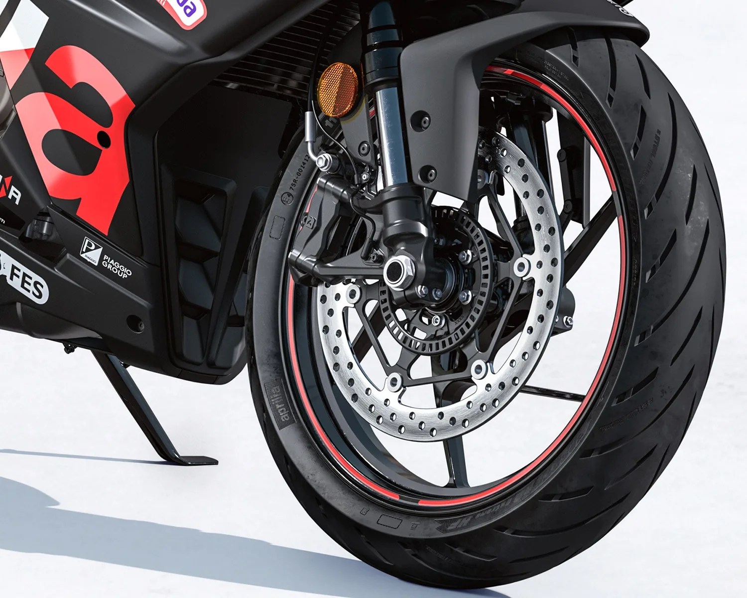 Front wheel of a black Aprilia motorcycle with red rim stripes and disc brake visible.
