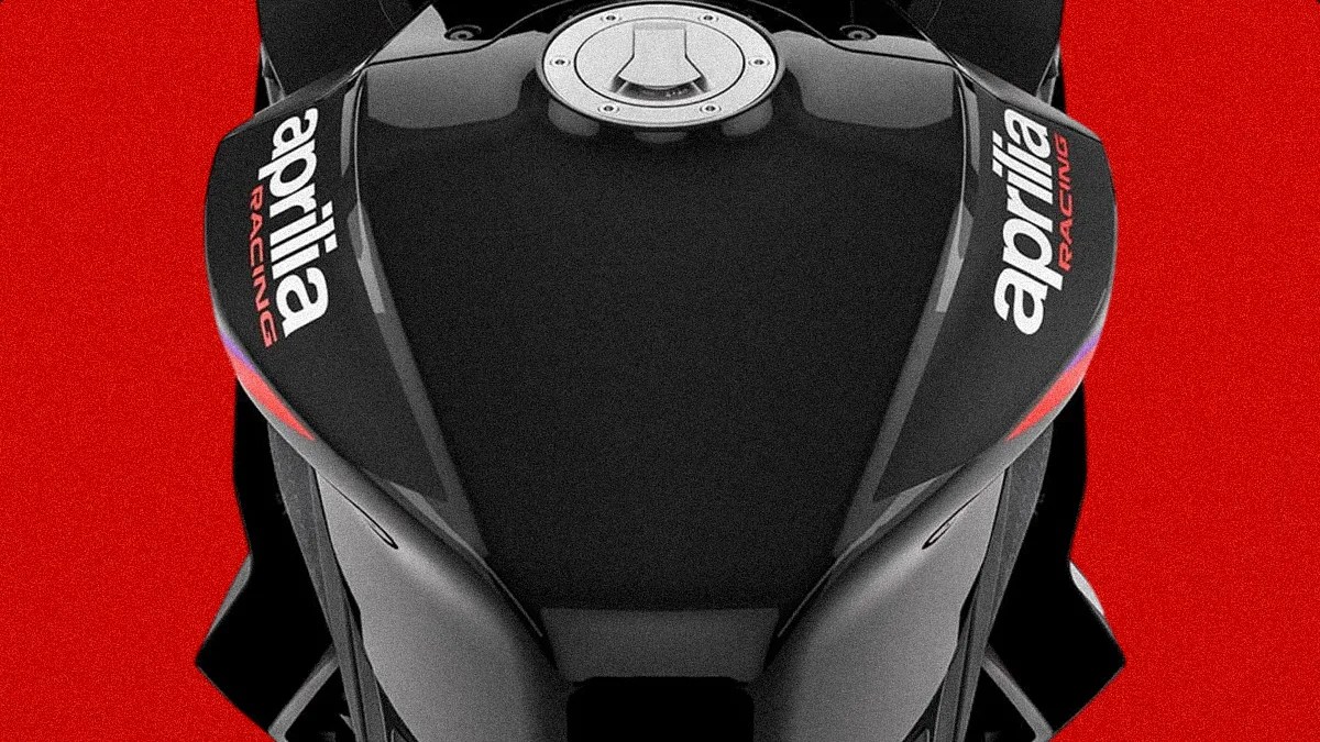 Close-up of a black Aprilia Racing motorcycle fuel tank against a red background.