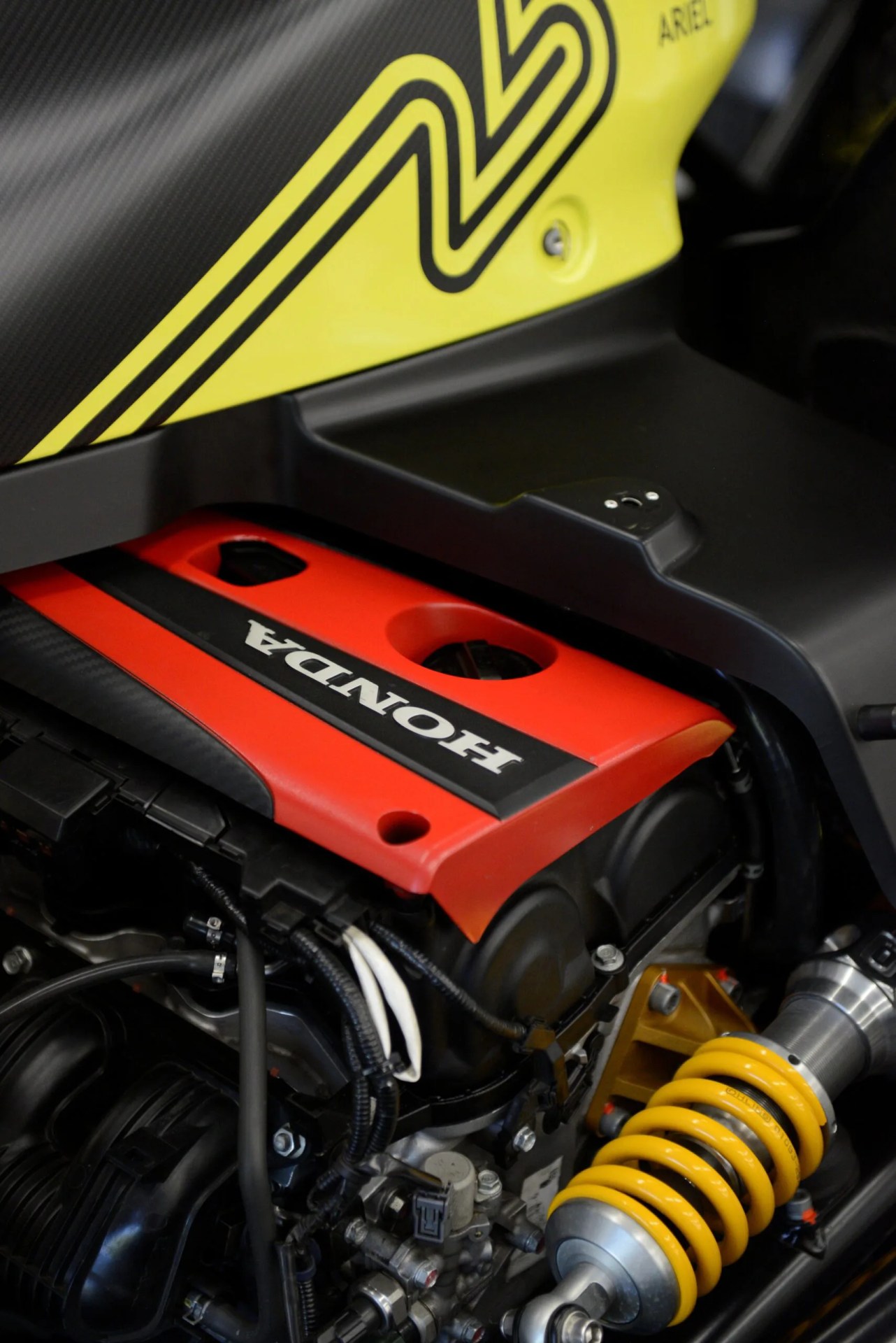 Close-up of a red Honda engine cover with black and white wiring and a yellow coil spring suspension component.