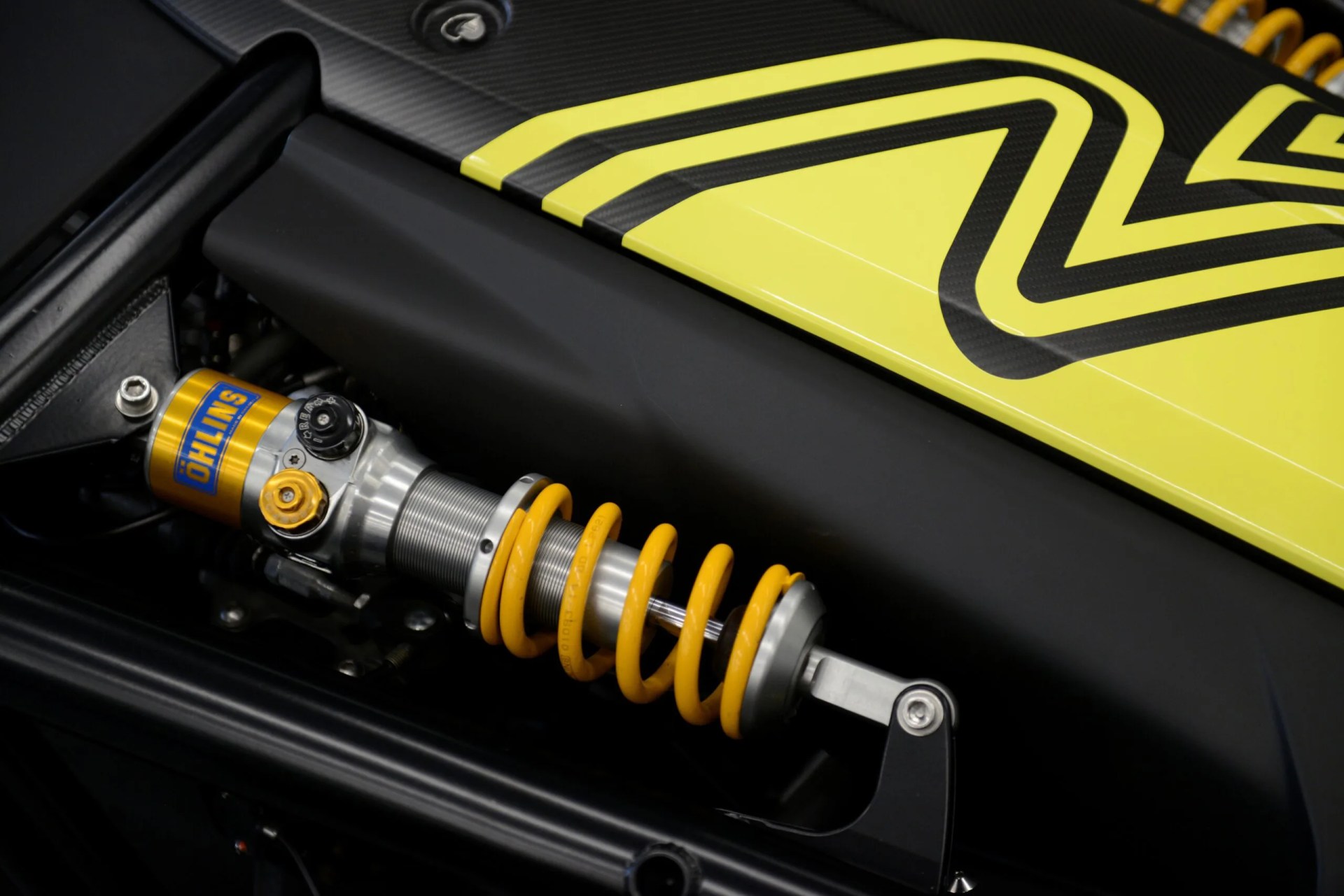Yellow coil spring shock absorber with Öhlins branding mounted on a black and yellow vehicle frame.