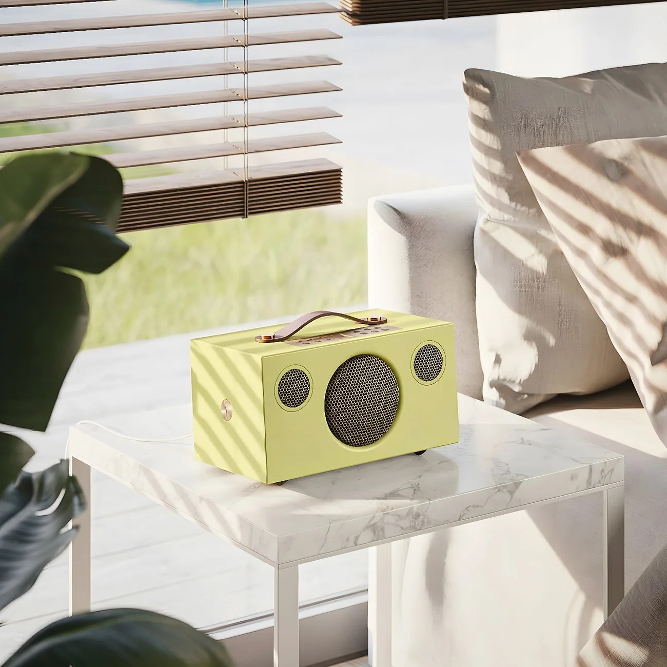 Yellow rectangular portable speaker with a leather handle on a white marble side table next to a beige sofa.