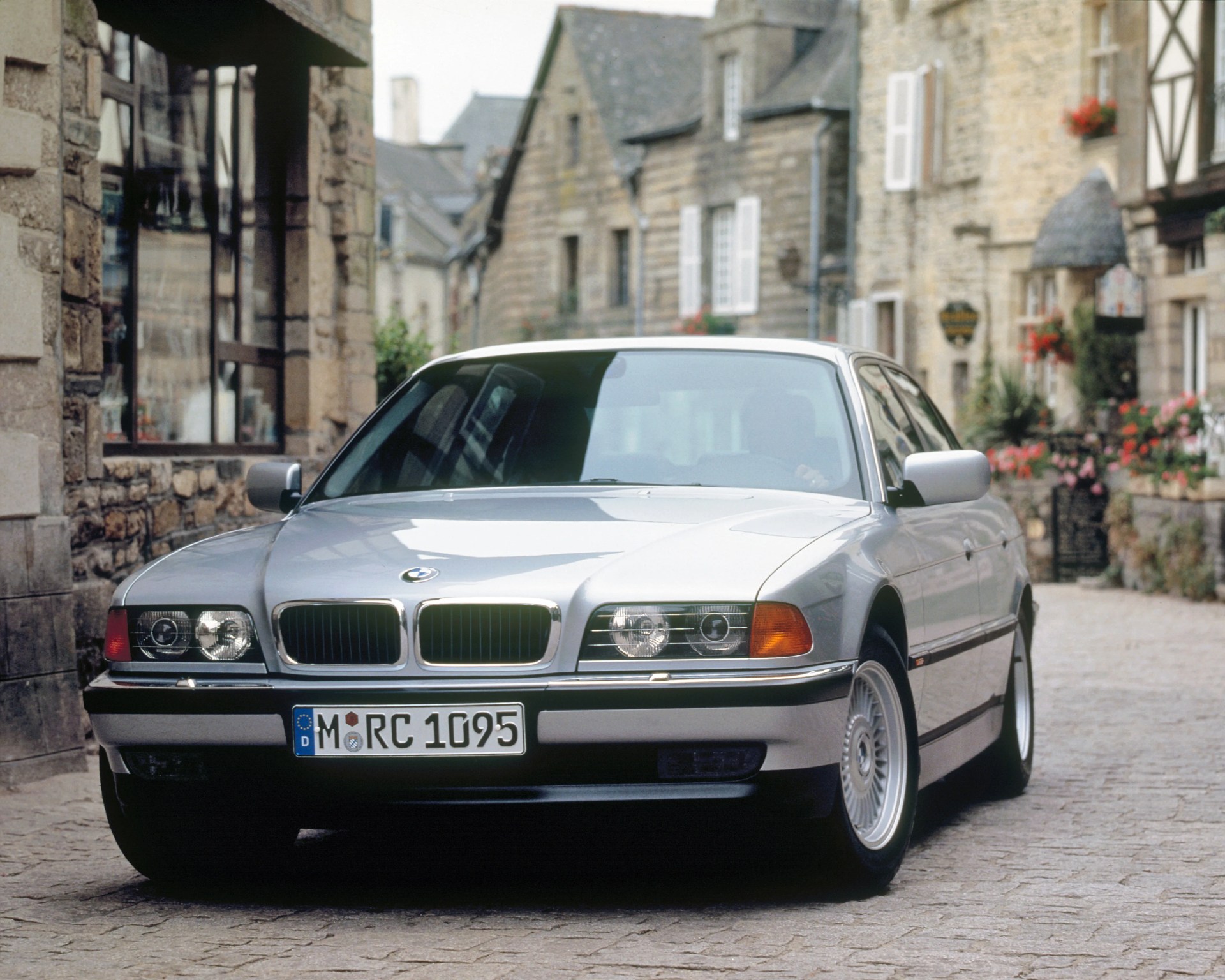Silver BMW sedan parked on a cobblestone street in front of stone buildings with flower boxes.