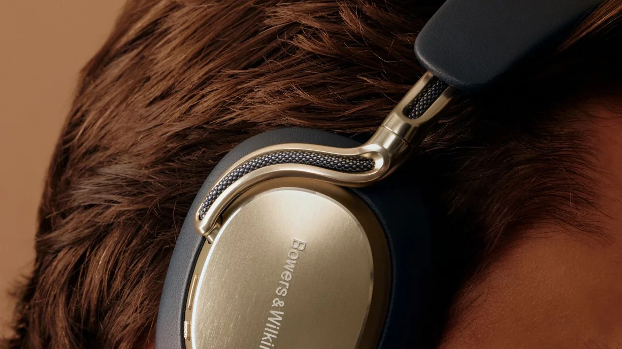 Close-up of gold and black Bowers & Wilkins over-ear headphones worn on a person's head.