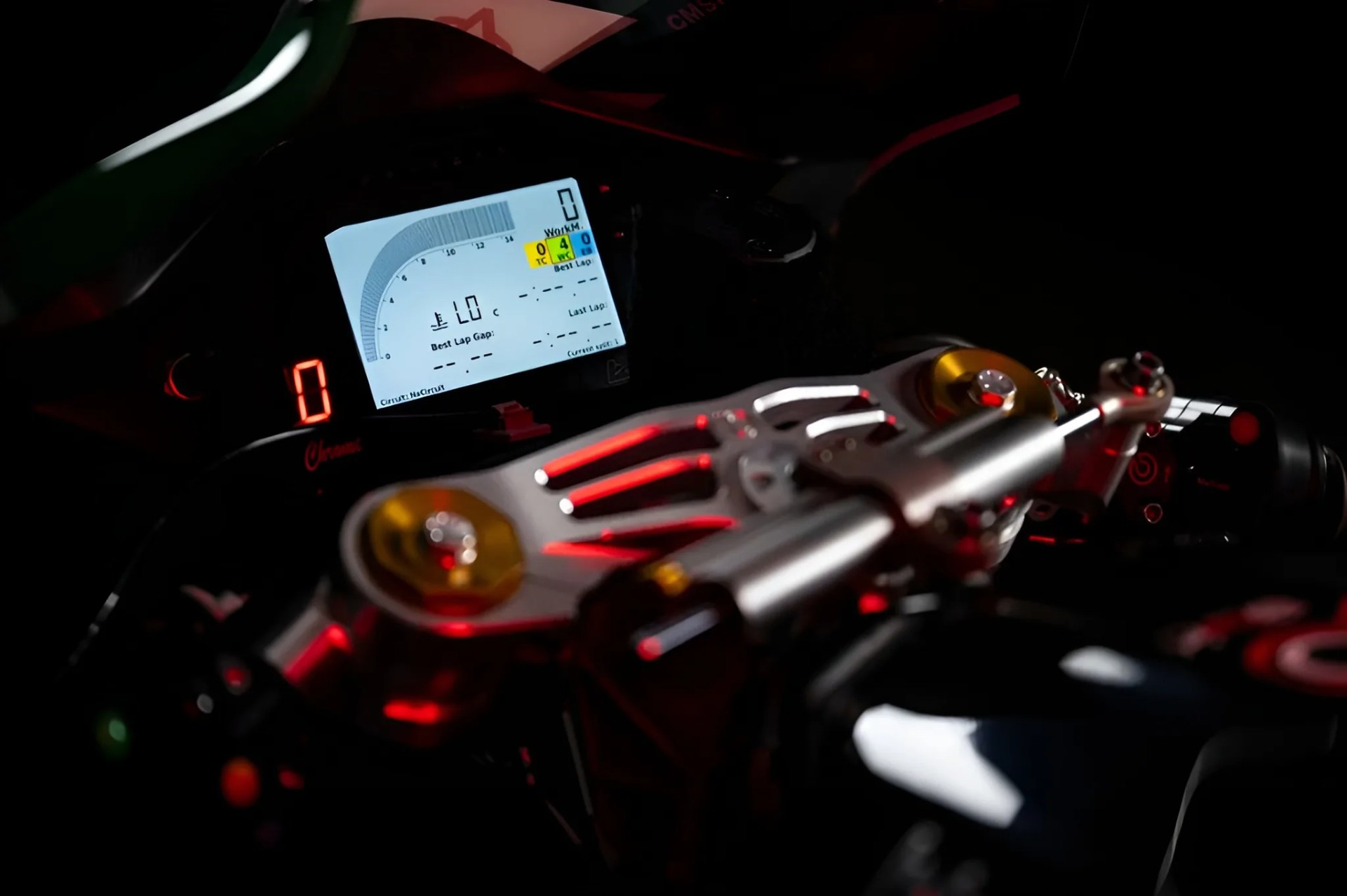 Close-up of a motorcycle digital dashboard with illuminated speedometer and metallic handlebar clamps with gold accents.