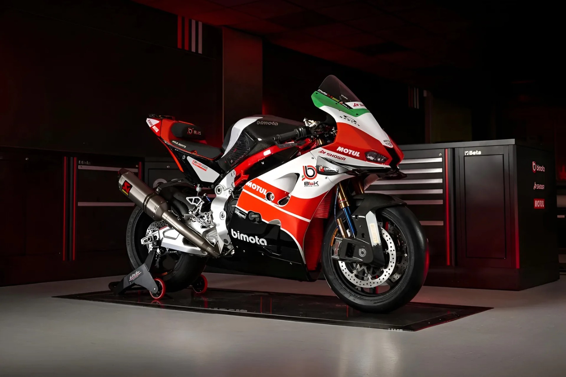 Red, white, and black Bimota sport motorcycle with green windshield on a rear stand in a garage.