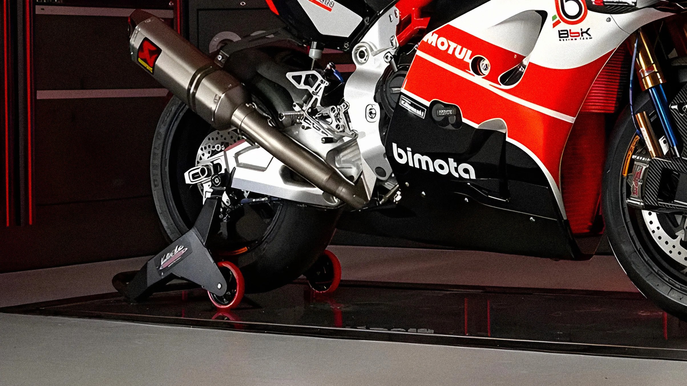 Close-up of a red, white, and black Bimota motorcycle exhaust and rear wheel on a black and red stand.