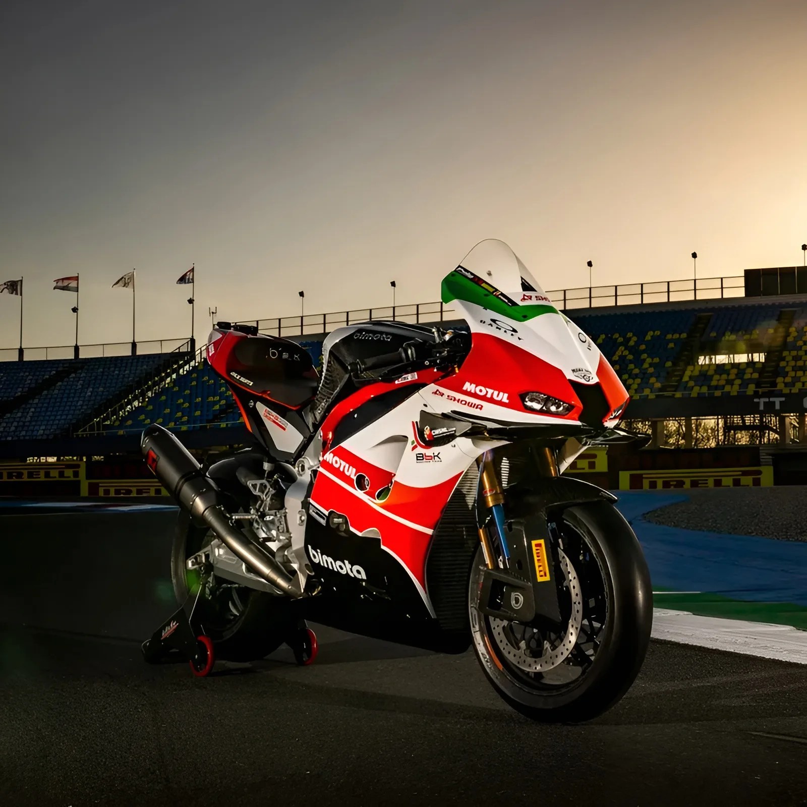Red, white, and black Bimota racing motorcycle on a track at sunset with Pirelli branding in the background.