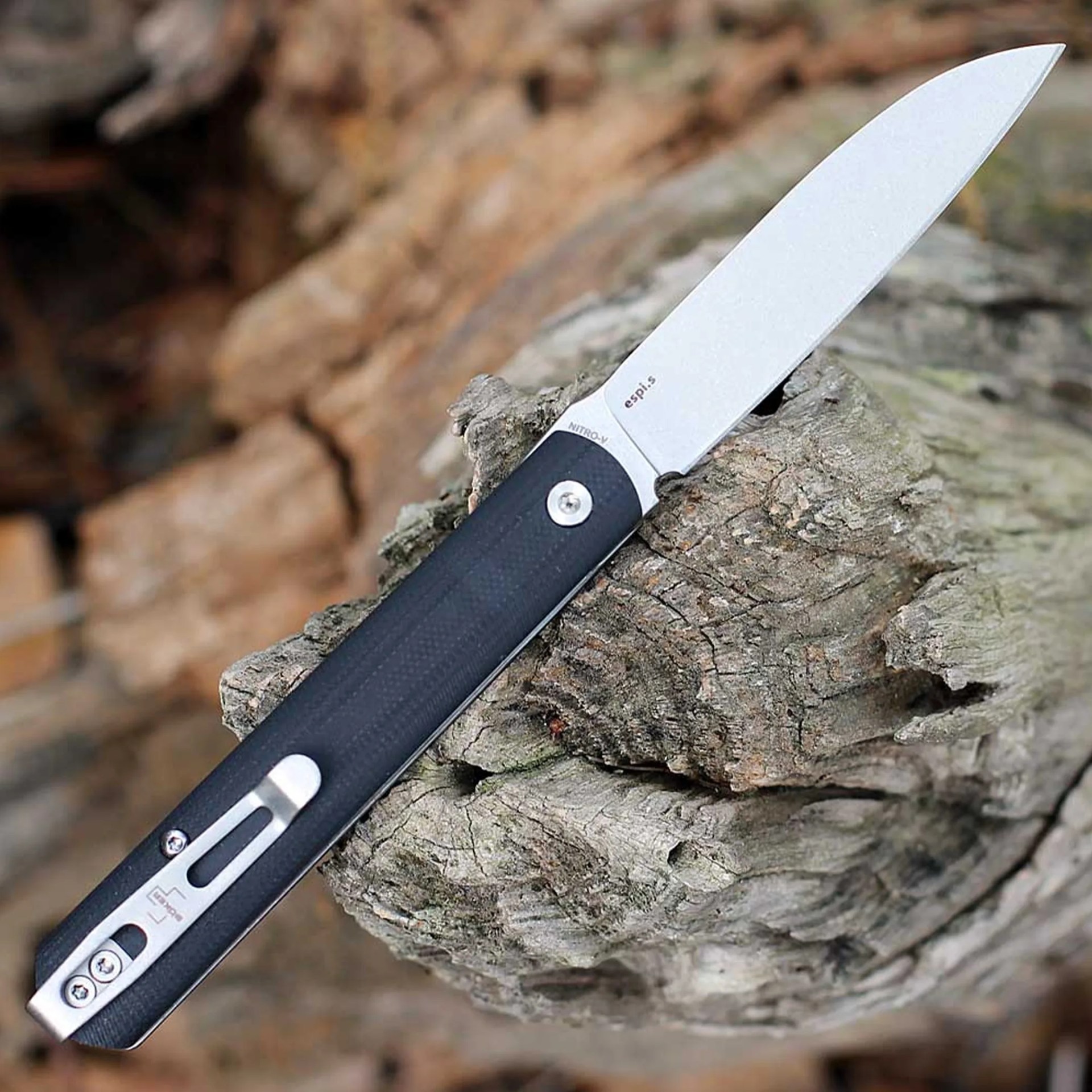 Folding knife with a silver blade and black textured handle resting on a piece of weathered wood.