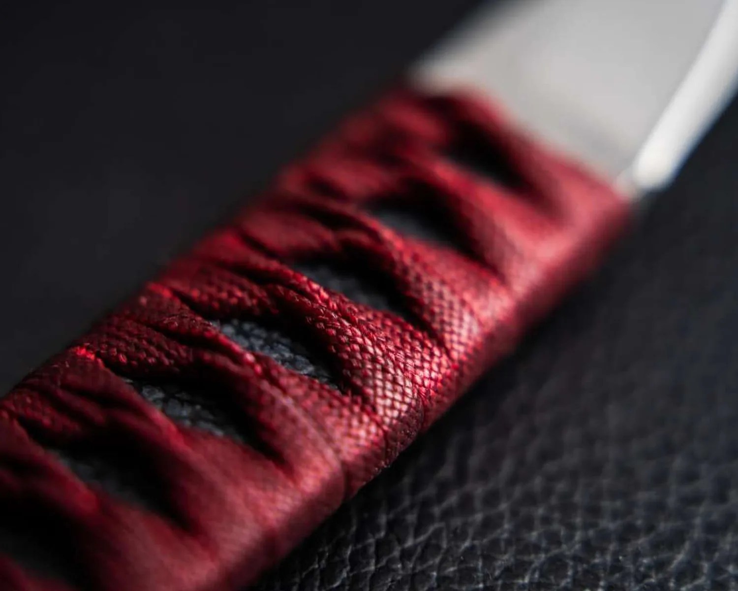 Close-up of a knife handle wrapped in textured red cord over a black textured surface.