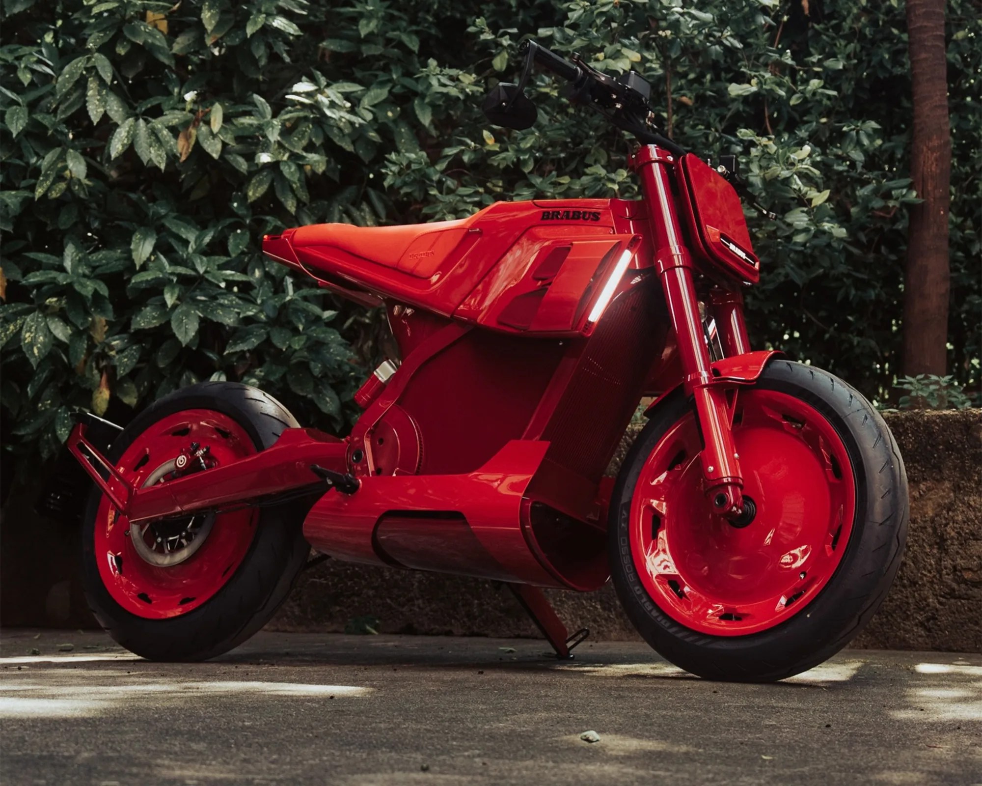 Red Brabus electric motorcycle with solid red wheels and sleek angular body parked outdoors.