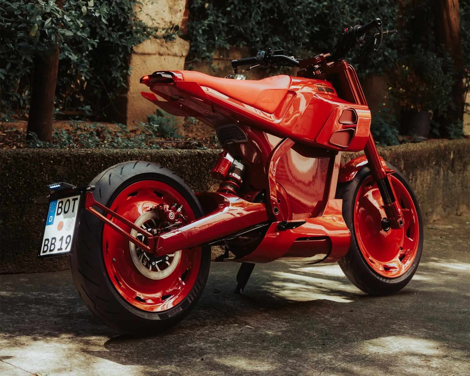 Glossy red futuristic motorcycle with wide tires and a visible rear suspension, parked on a paved surface.