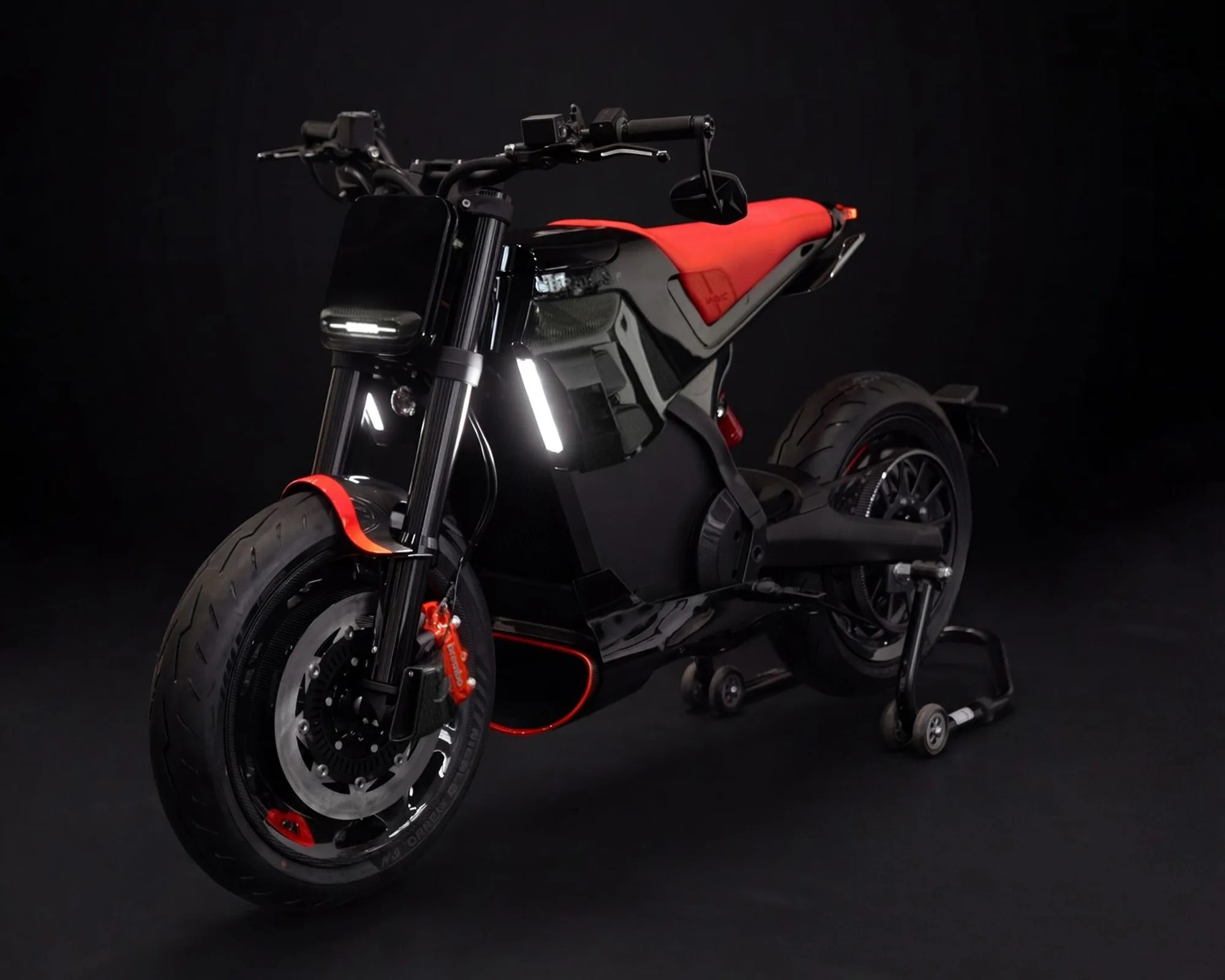 Black electric motorcycle with red seat and red accents on tires and brake calipers against a dark background.