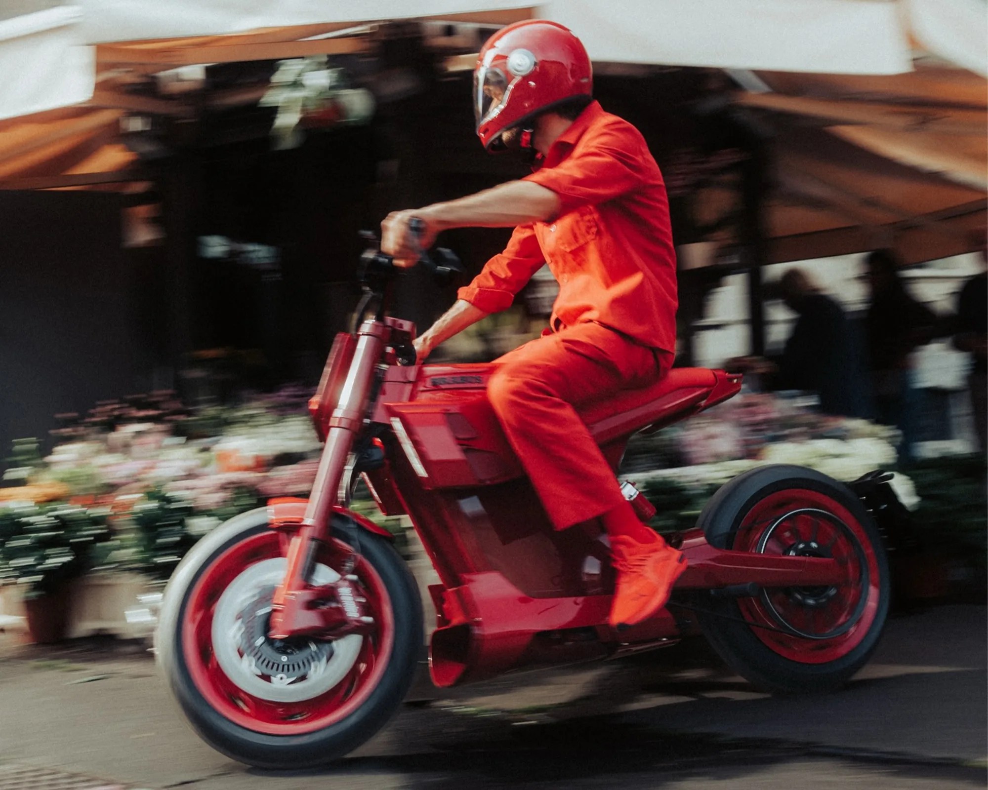 Person in red helmet and outfit riding a red electric motorcycle with blurred background.
