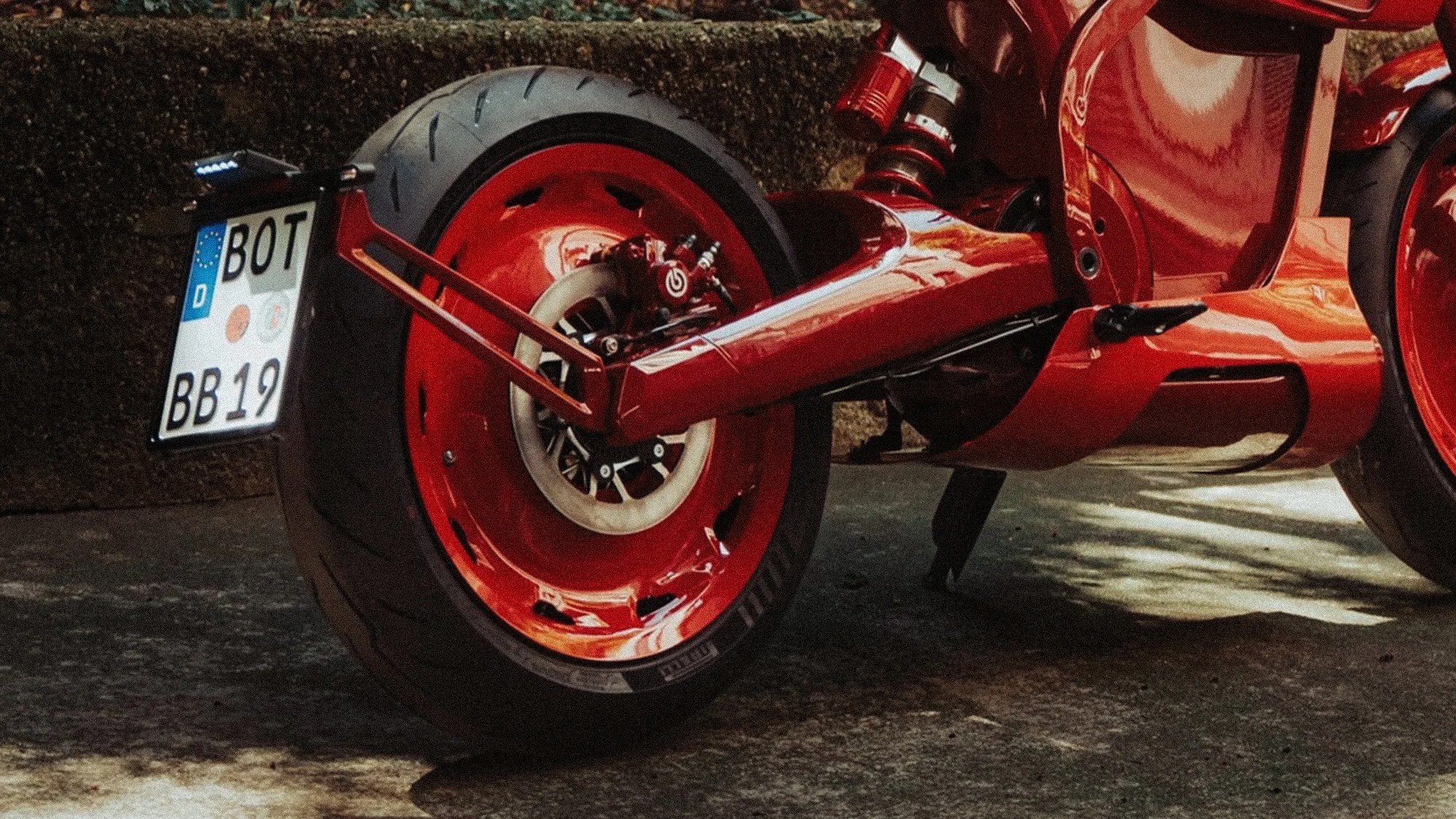 Rear view of a red motorcycle with a wide tire, Brembo brake caliper, and a European license plate.