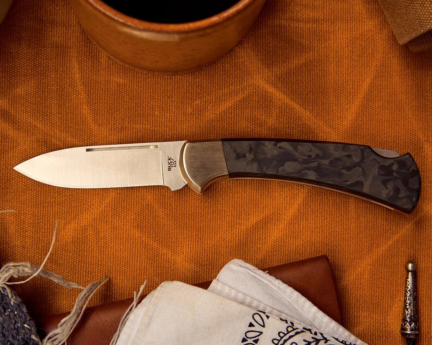 Folding knife with a brushed steel blade and dark marbled handle on an orange fabric surface.
