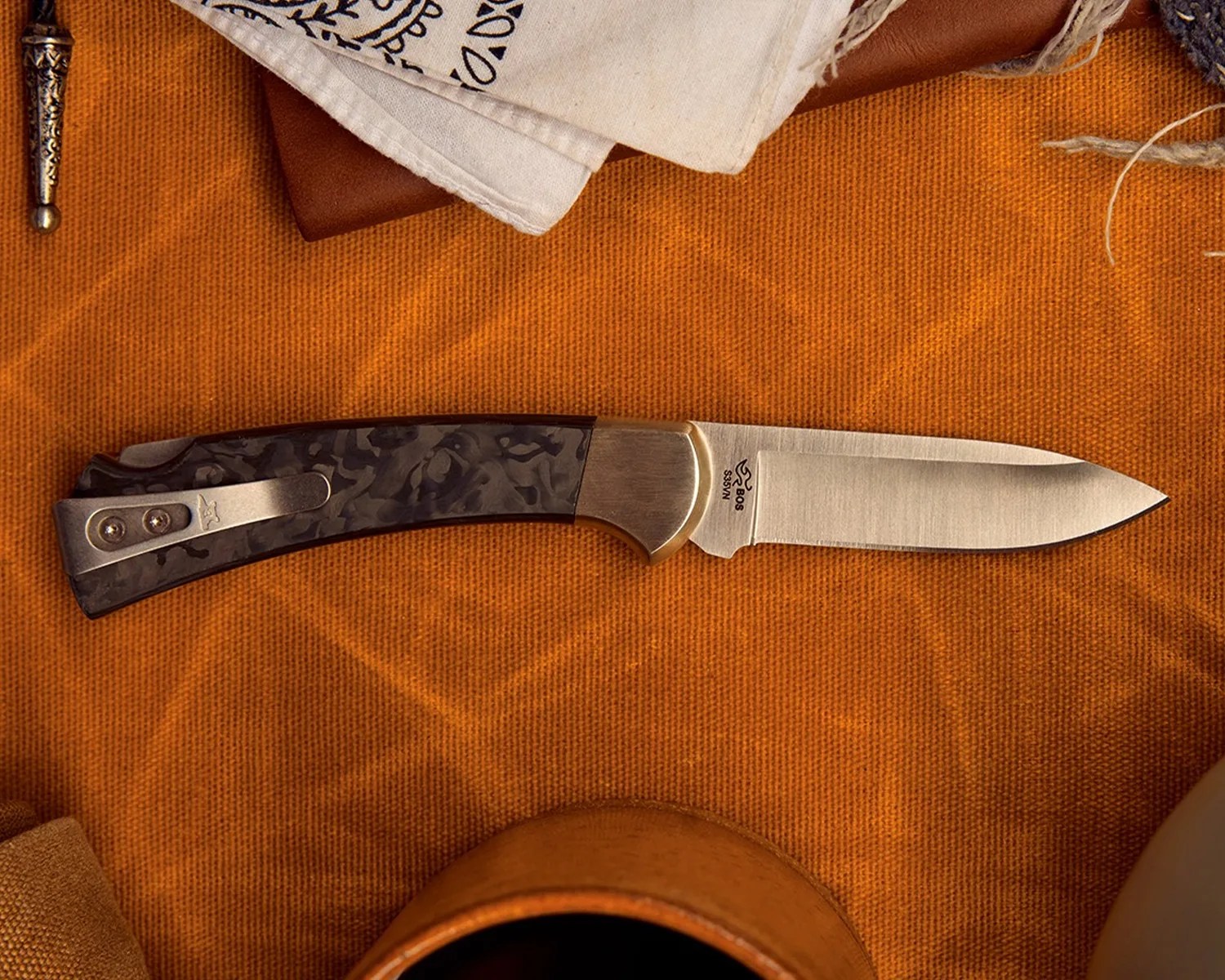 Folding knife with a patterned dark handle and a stainless steel blade on an orange textured surface.