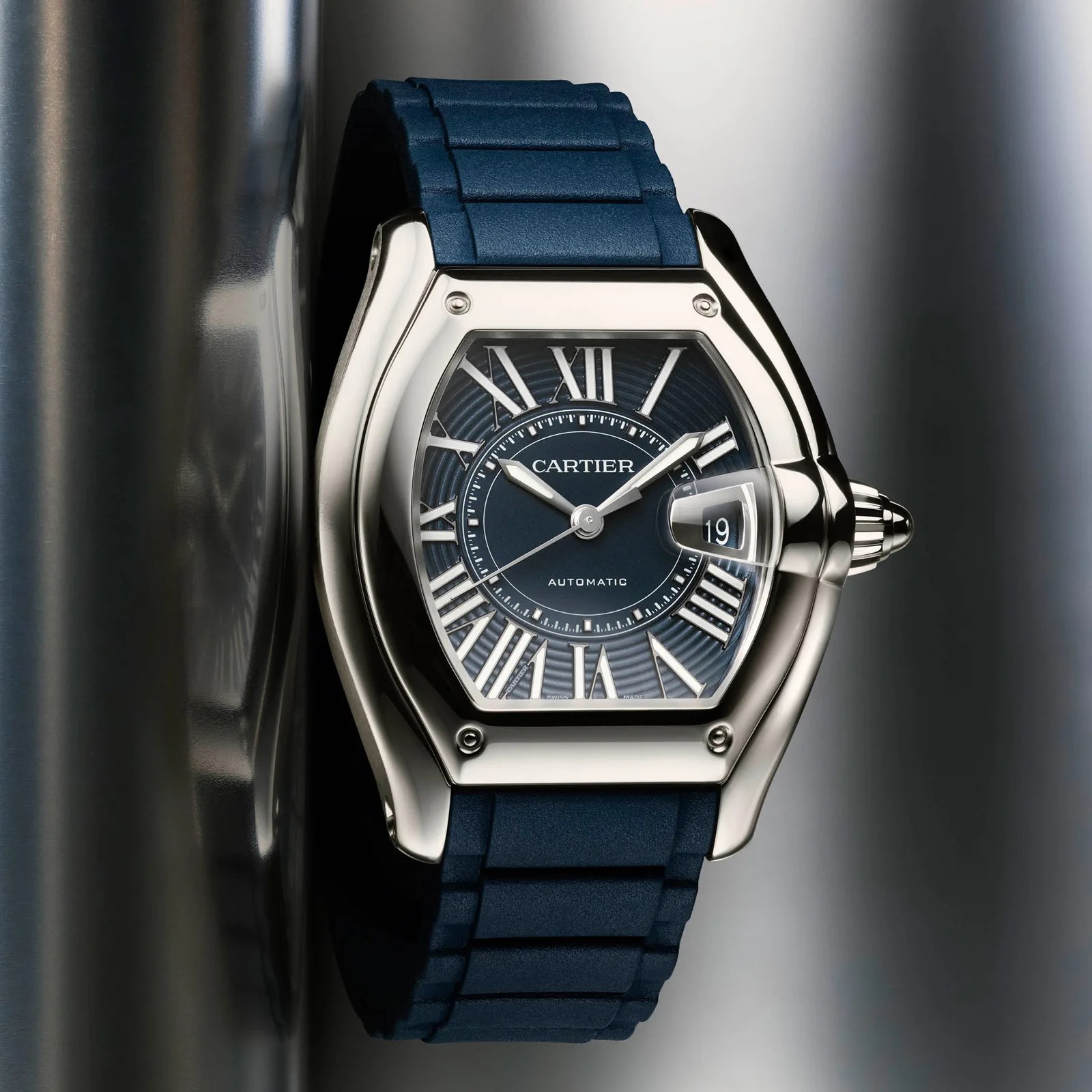 Cartier wristwatch with a blue rubber strap, silver case, and blue dial featuring Roman numerals and date display.