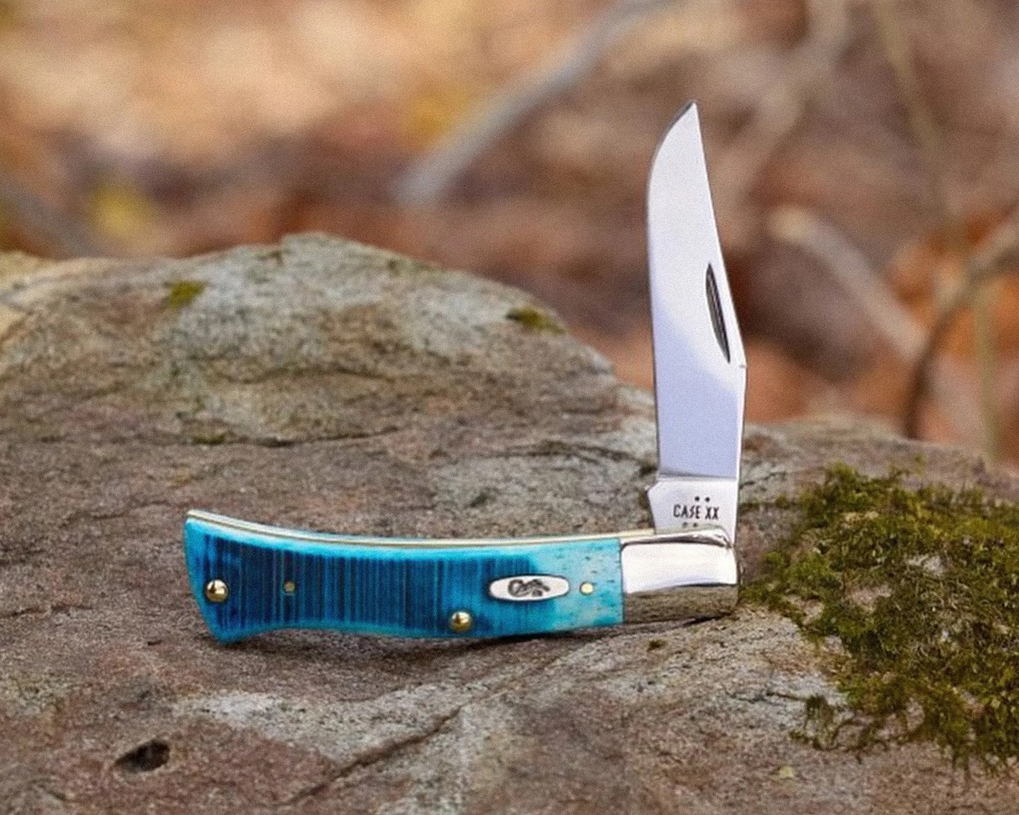 Blue-handled folding pocket knife with a partially open blade resting on a rock.