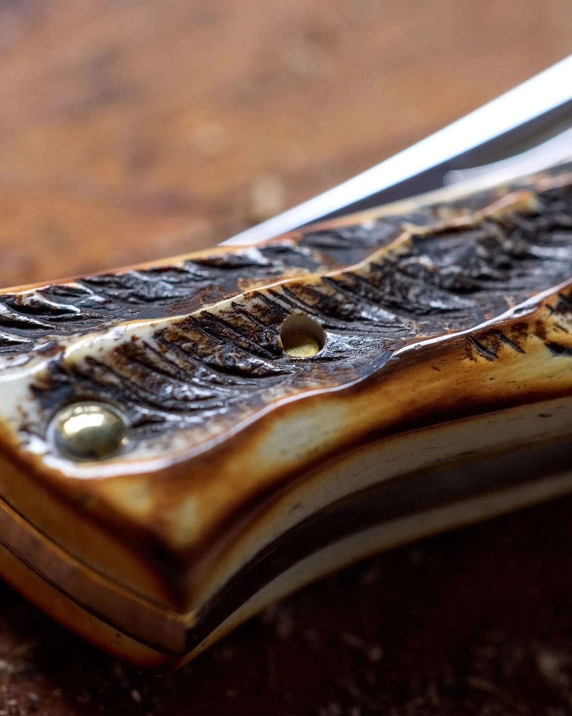 Close-up of a carved wooden knife handle with a brass rivet and a hole, showing detailed texture.