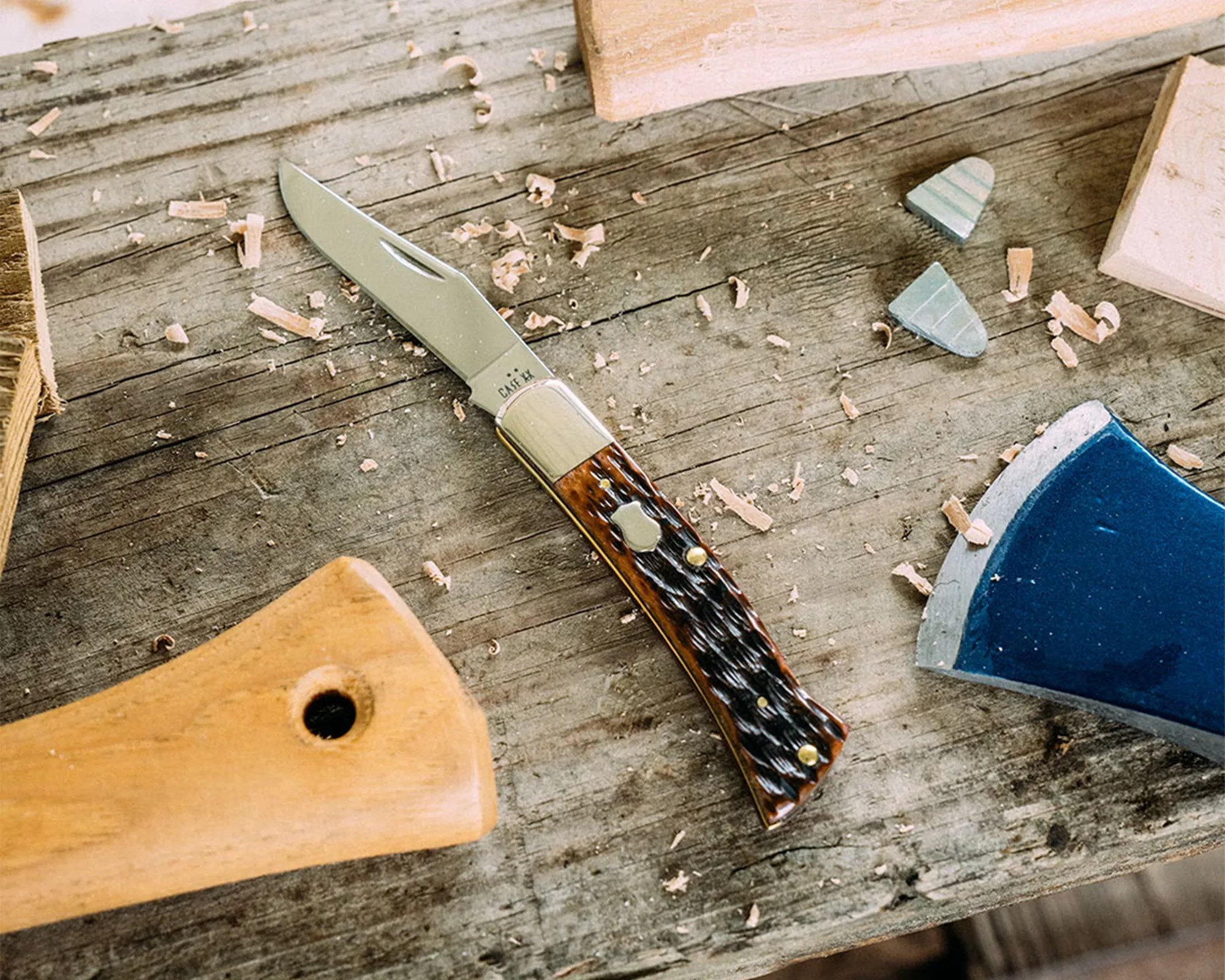 Folding pocket knife with a brown textured handle and silver blade on a wooden workbench with wood shavings.