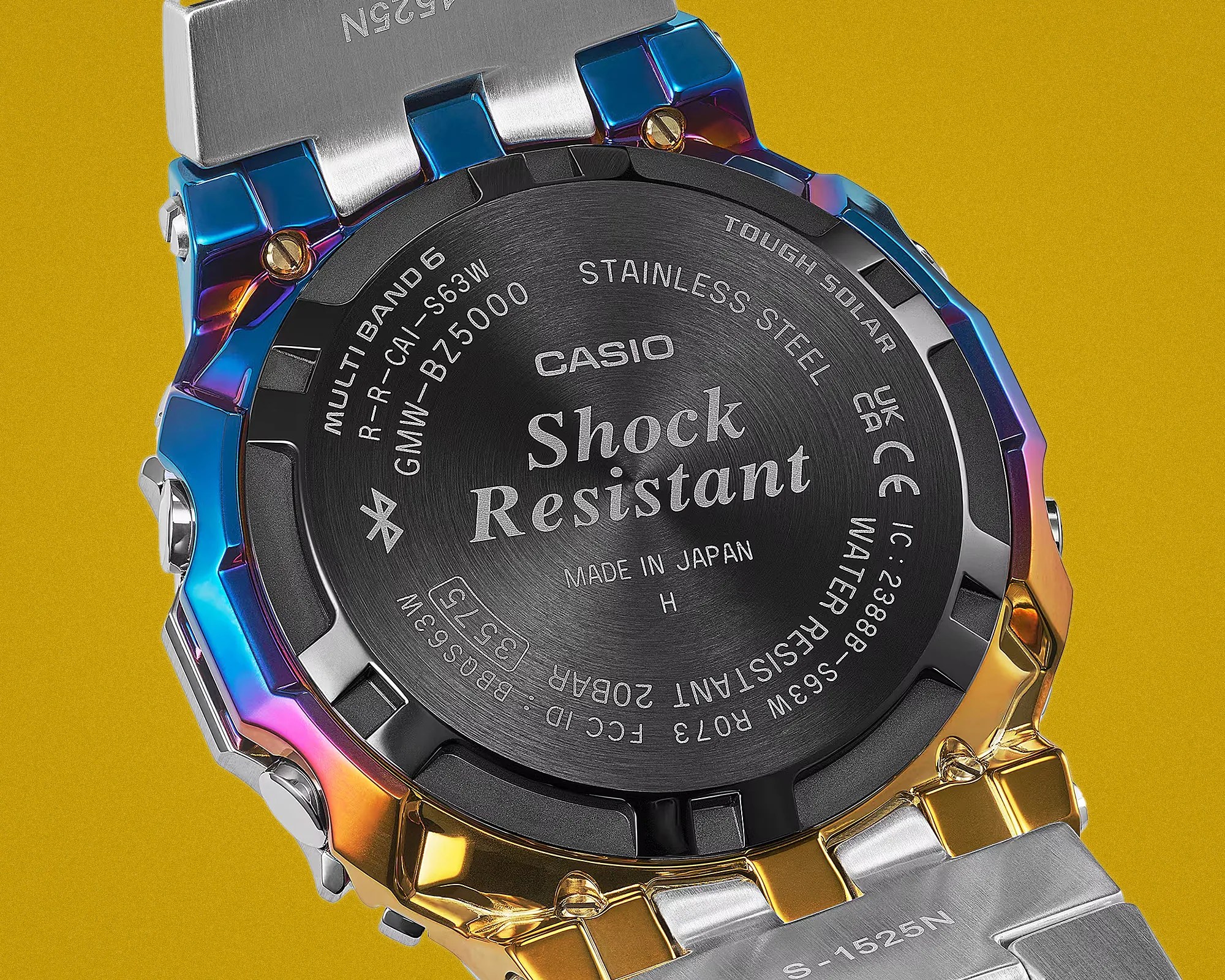 Back of a Casio G-Shock watch with multicolor metal casing and stainless steel band on a yellow background.