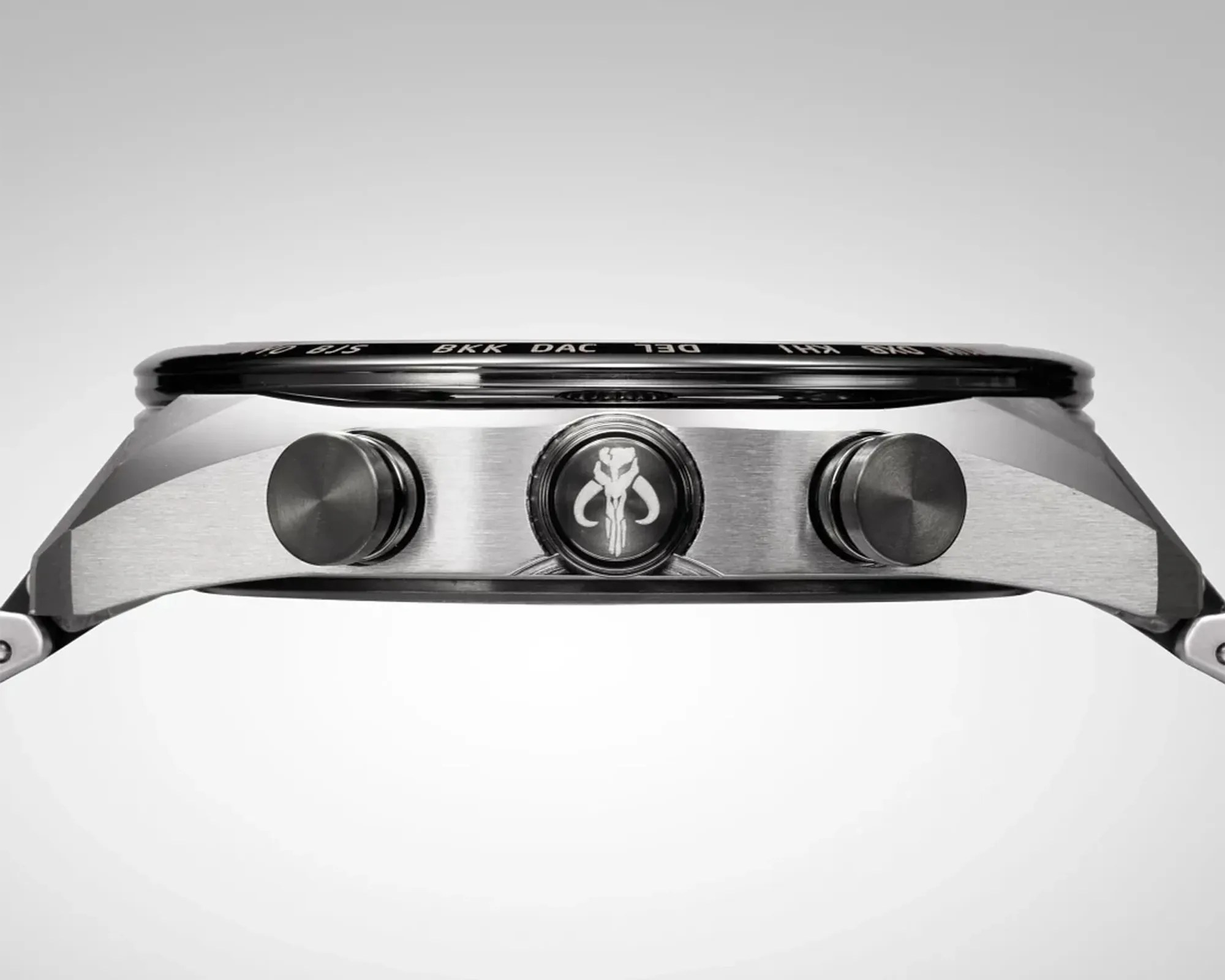 Side view of a stainless steel watch case with three black pushers, one featuring a Mandalorian skull emblem.