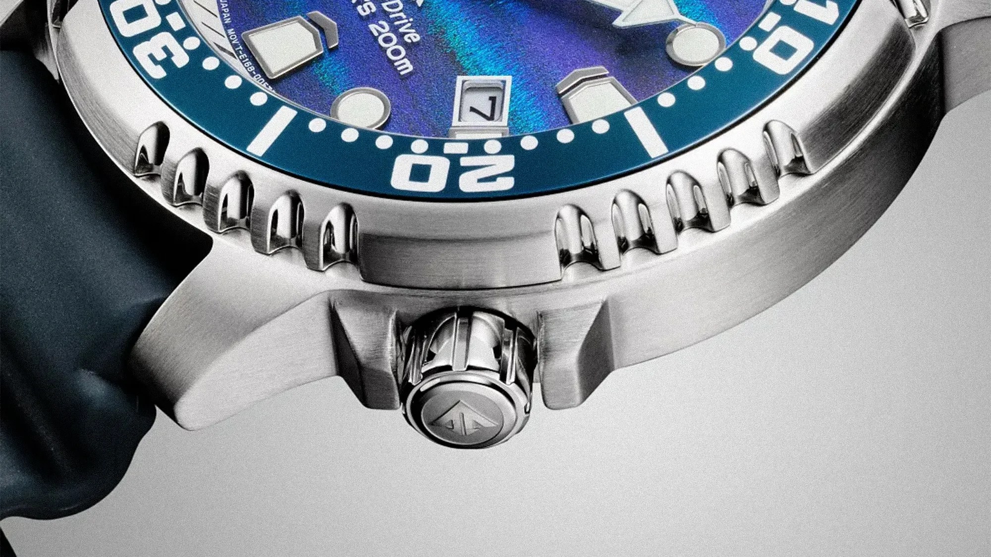 Close-up of a stainless steel watch case with a blue bezel, crown with logo, and part of a blue strap.