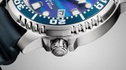 Close-up of a stainless steel watch case with a blue bezel, crown with logo, and part of a blue strap.