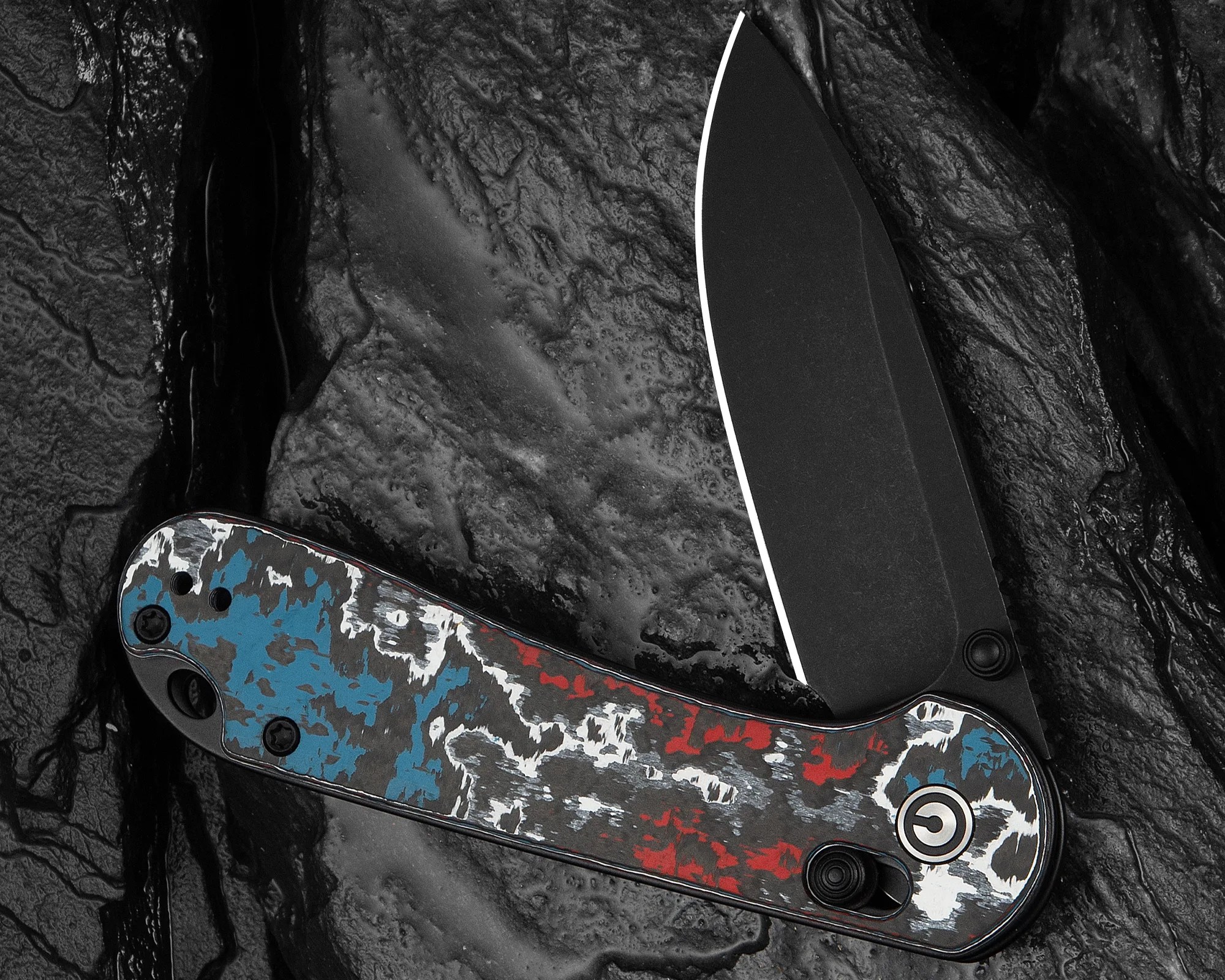 Folding knife with black blade and handle featuring a red, white, and blue distressed pattern on a textured black surface.