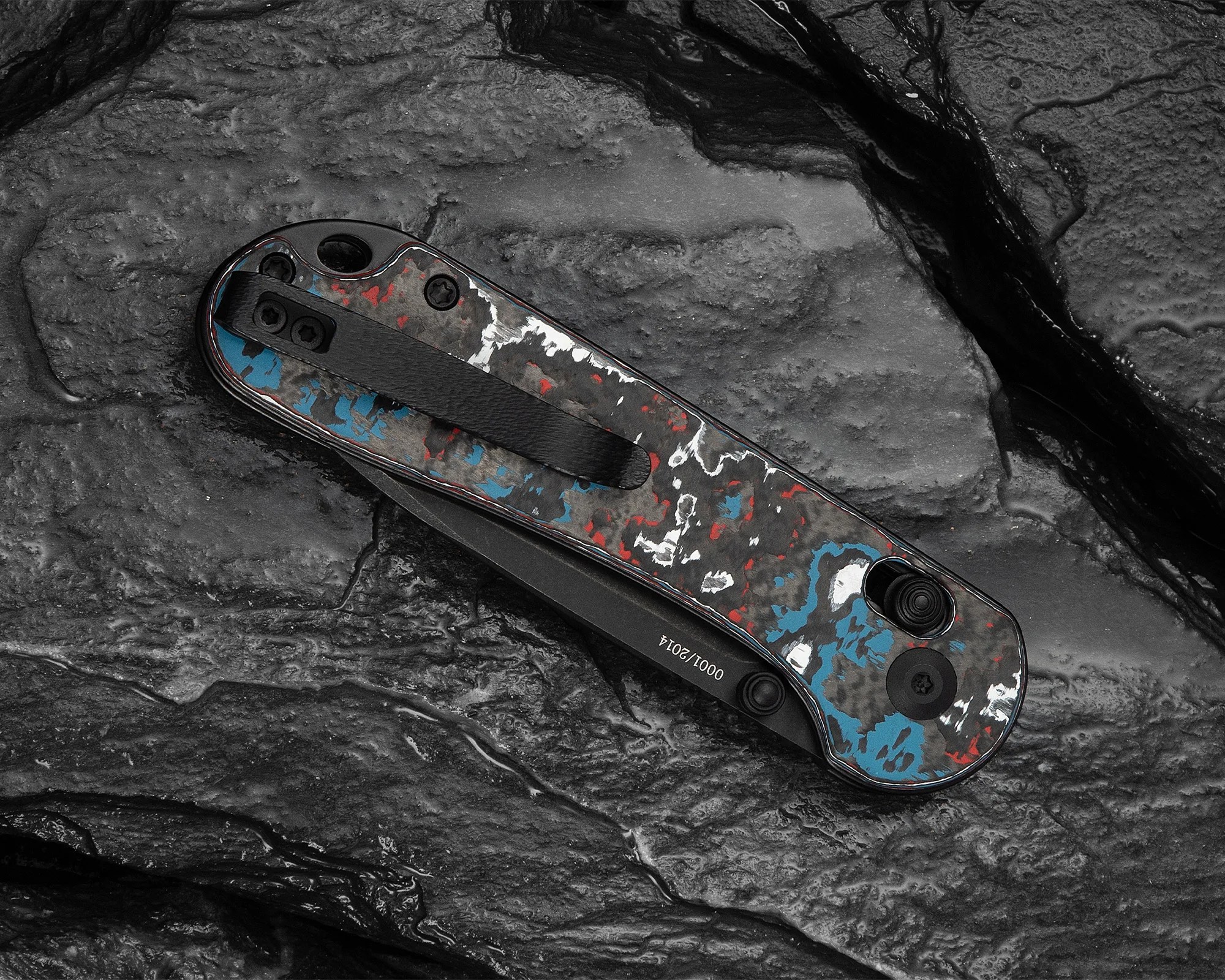 Folded pocket knife with a black clip and a multicolored handle featuring red, blue, and white patterns on a textured dark surface.