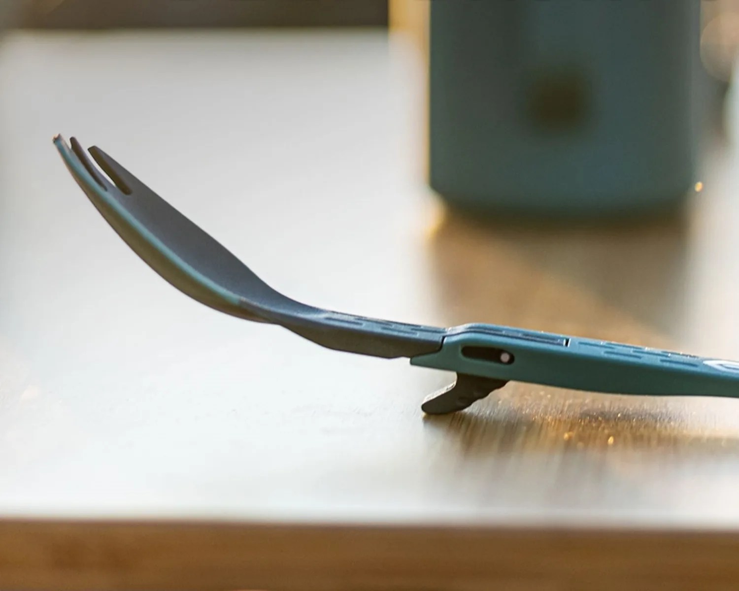 Blue and black camping spork with a foldable handle resting on a wooden surface.