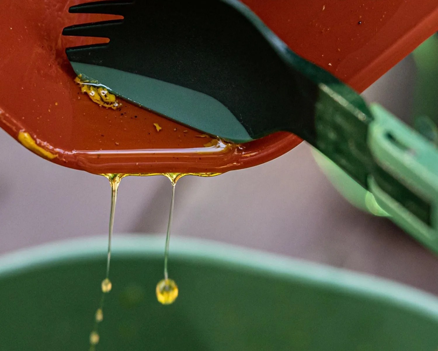 Close-up of honey dripping from an orange container held by a green and black utensil.