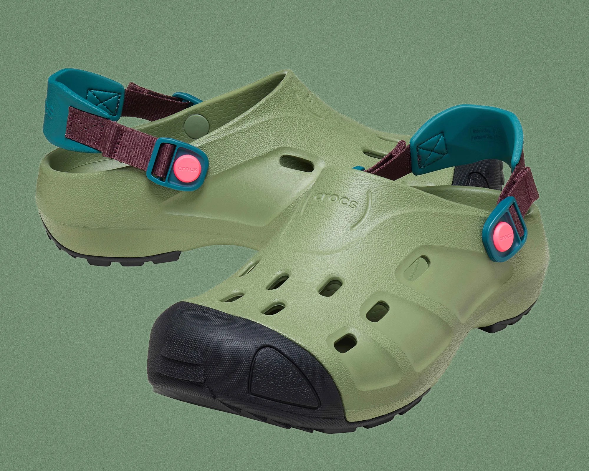 Green Crocs with black toe caps, teal heel straps, and maroon adjustable bands with pink buttons.