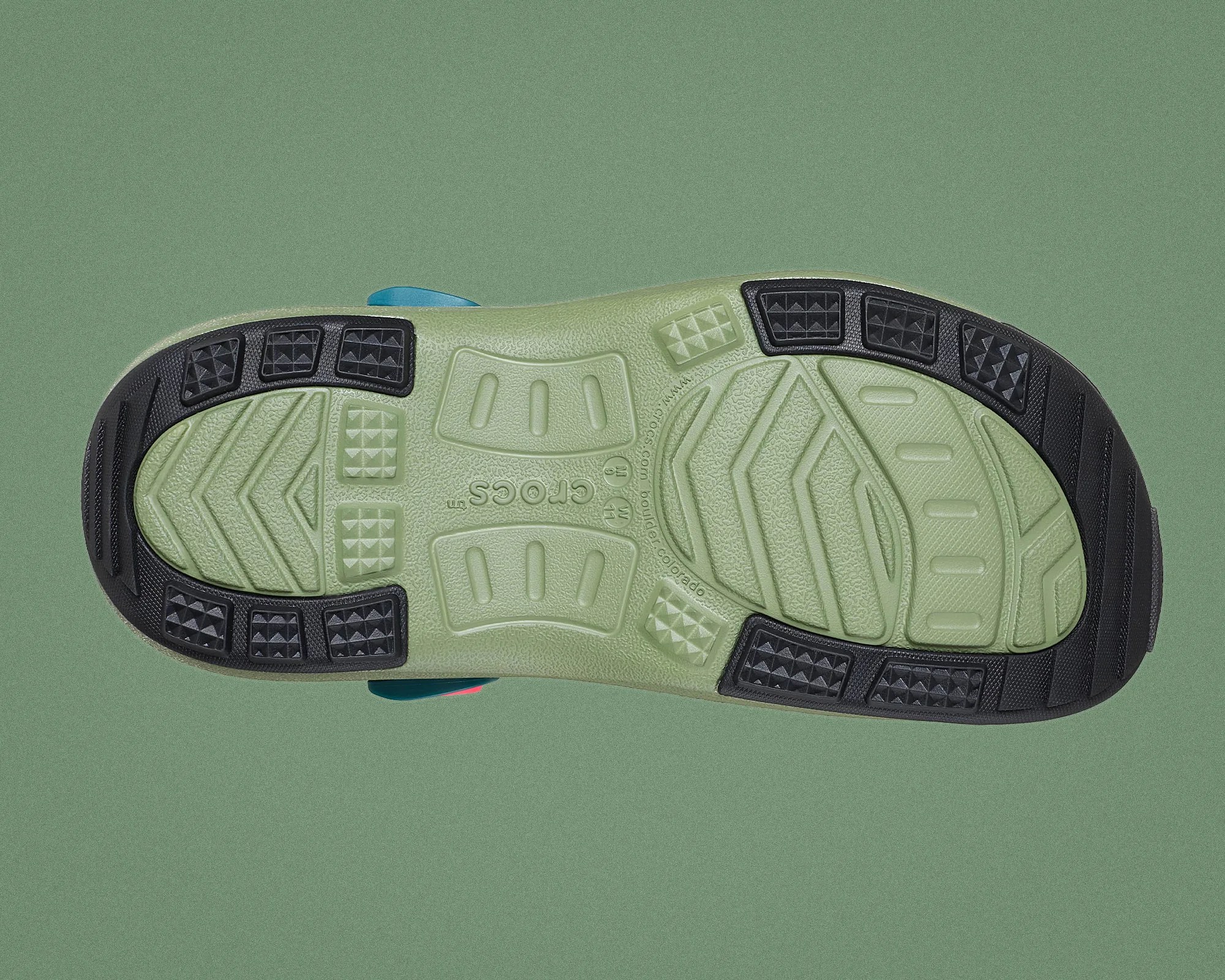 Light green Crocs shoe sole with black textured grip pads on a green background.