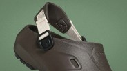 Close-up of a dark brown textured Crocs clog with an adjustable beige fabric strap and black buckle.