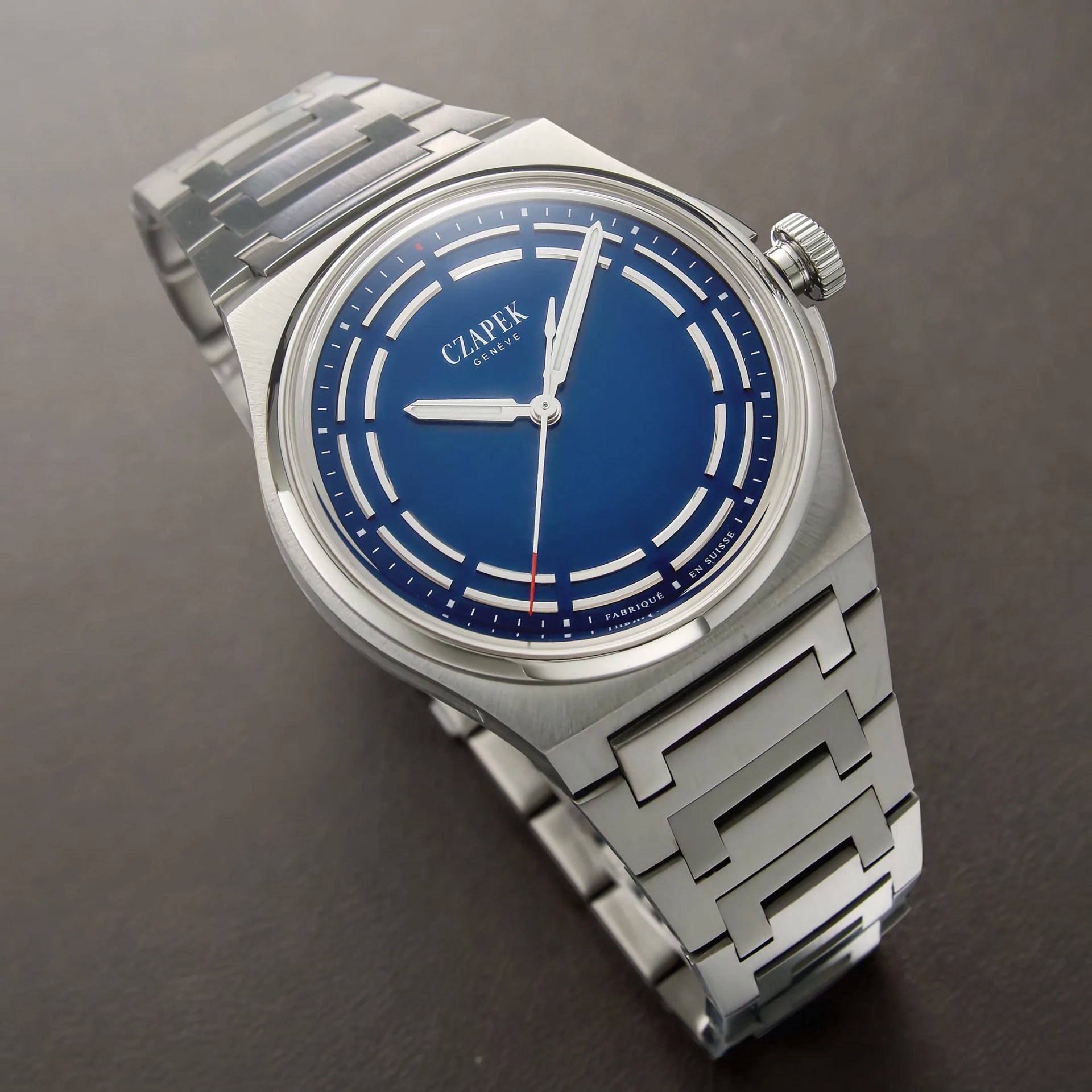 Silver titanium wristwatch with a blue dial and geometric link bracelet on a dark surface.