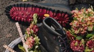 Black hiking boots with red and black laces and red Vibram soles surrounded by pink flowers and green leaves.