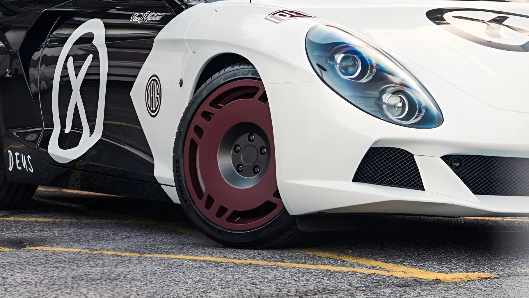 Close-up of a white and black sports car front with maroon disc-style wheel and dual round headlights.