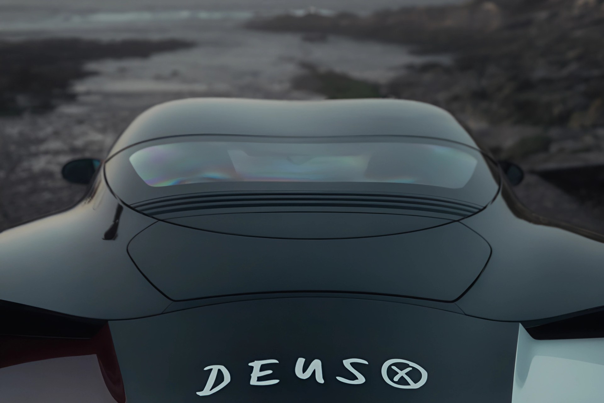 Rear view of a sleek black car with a curved rear window and the word "DEUS" on the back.
