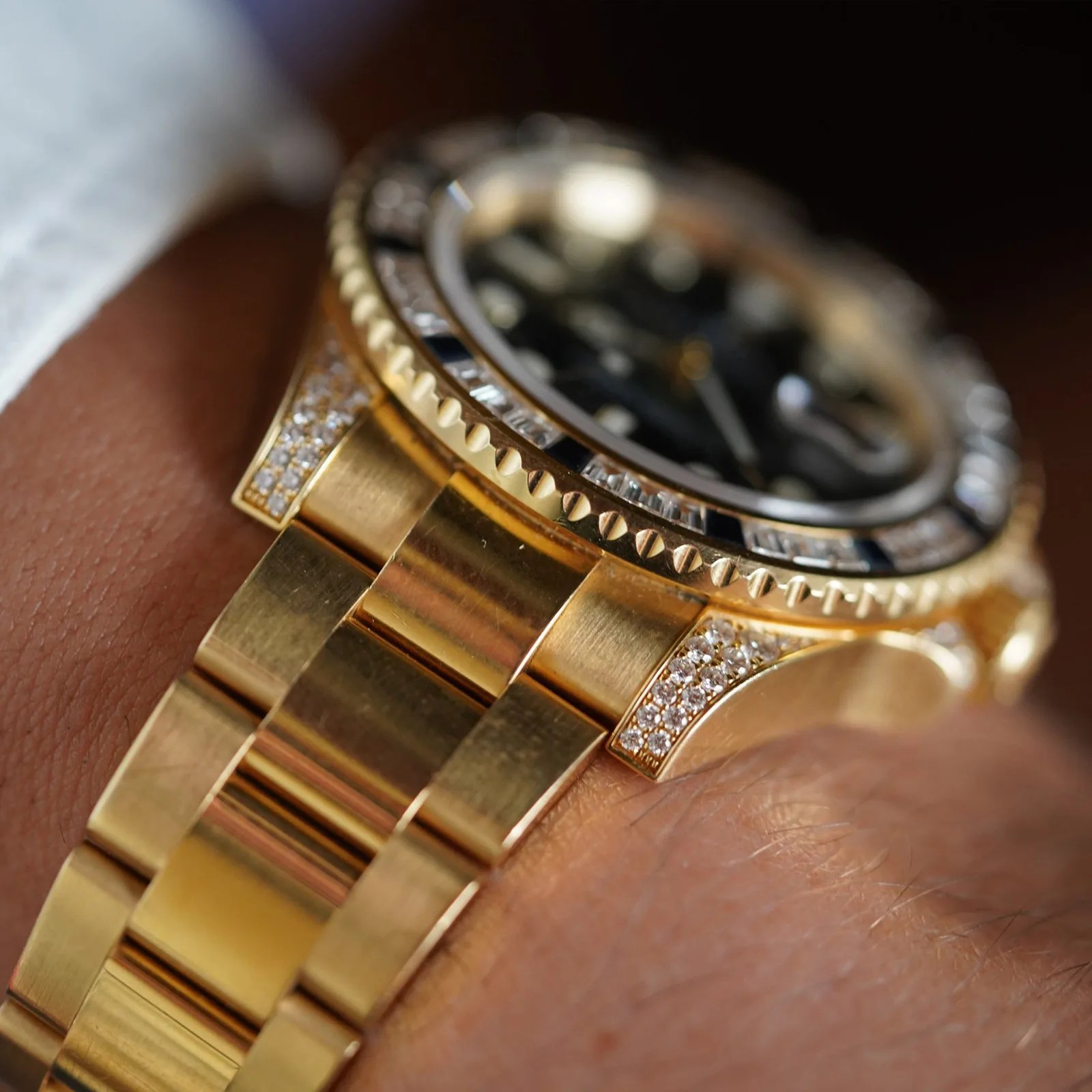 Close-up of a gold wristwatch with diamond accents on the bezel and bracelet links, worn on a wrist.
