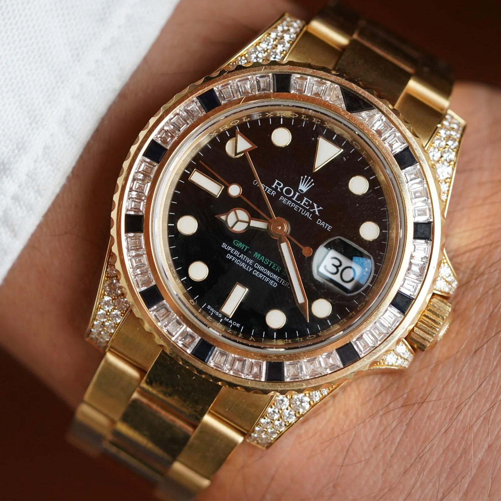 Gold Rolex GMT-Master II watch with black dial, diamond and sapphire bezel, and date display on wrist.