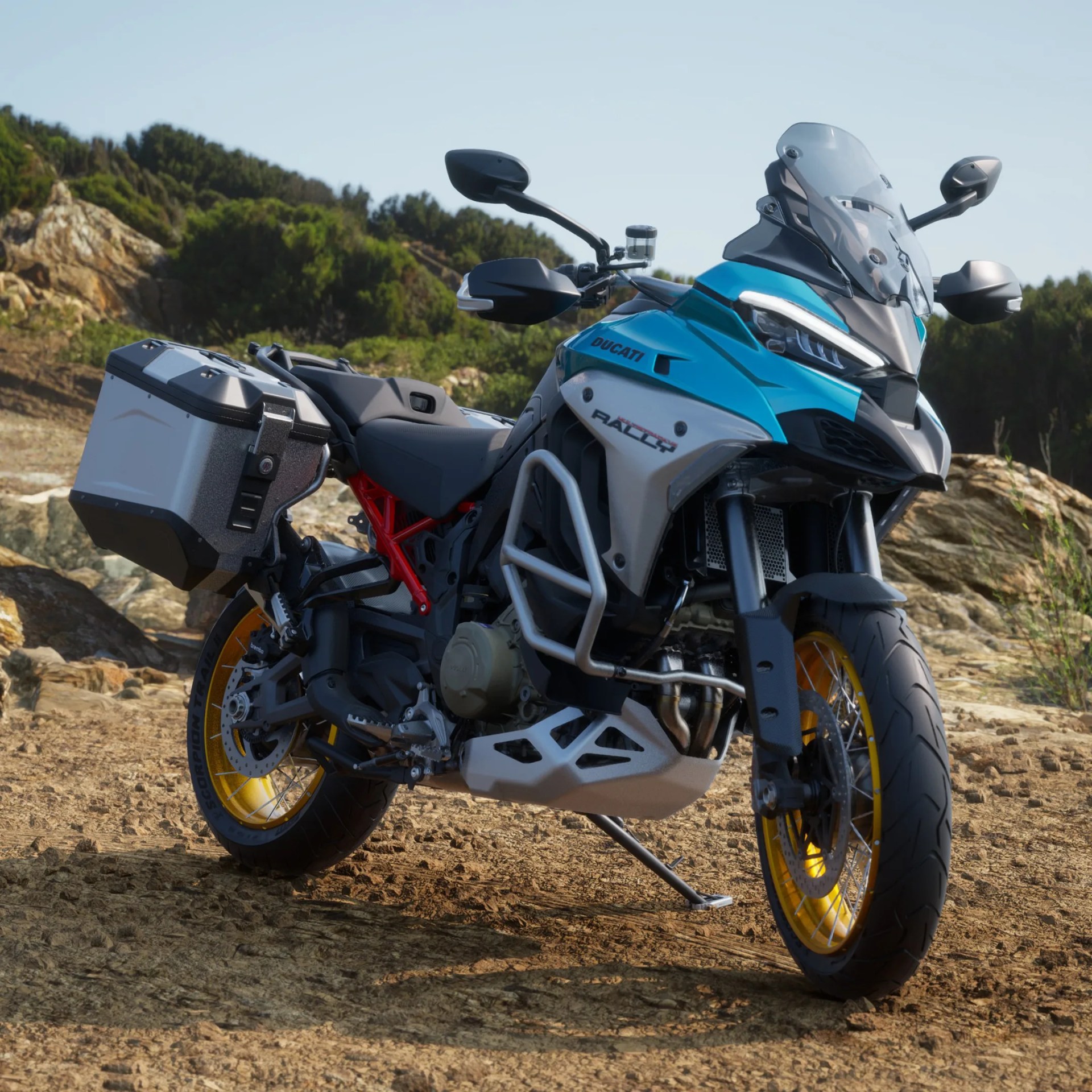 Blue and white Ducati Rally motorcycle with yellow rims and side panniers on a dirt trail.