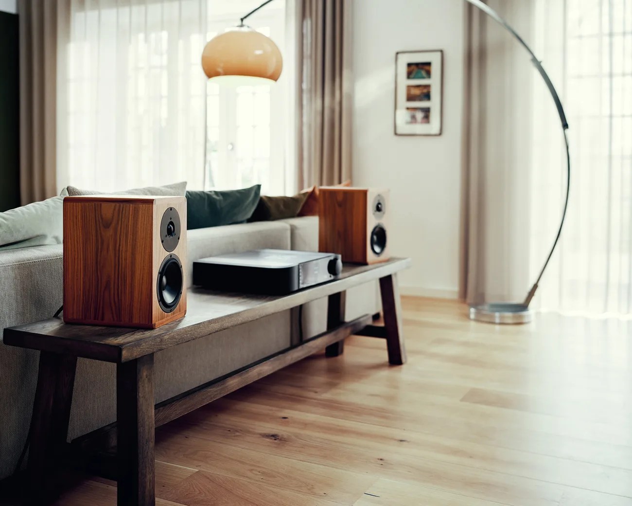 Pair of wooden bookshelf speakers and a black audio receiver on a wooden bench in a living room.