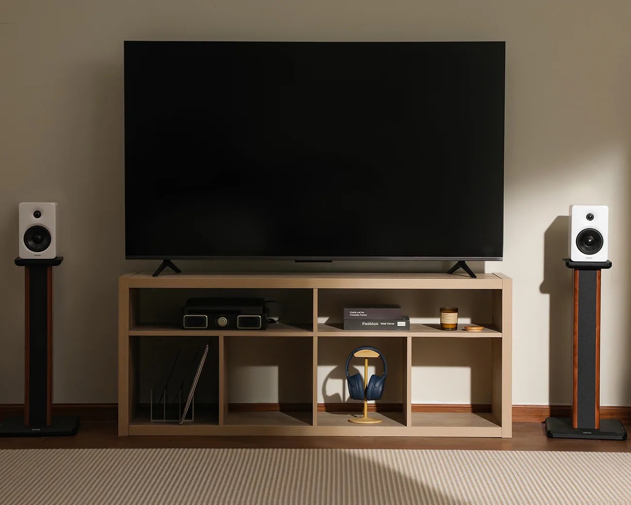 Flat-screen TV on a light wood media console with black and wood floor-standing speakers on each side.
