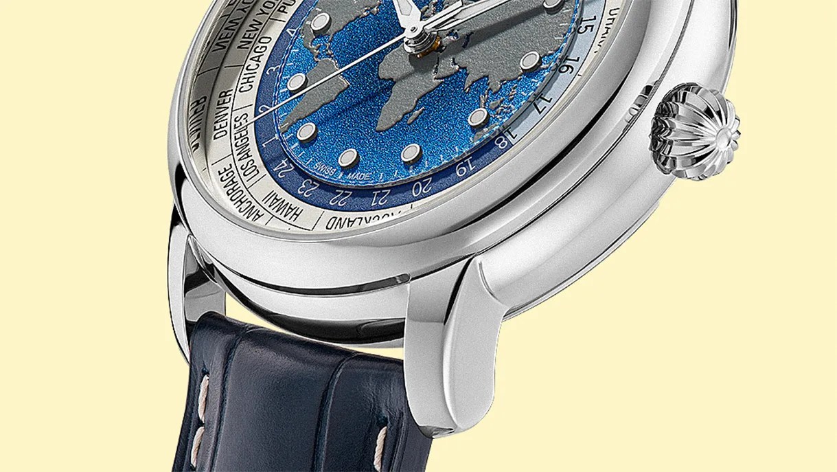 Close-up of a silver watch with a blue and gray world map dial, city names on the bezel, and a dark blue leather strap.