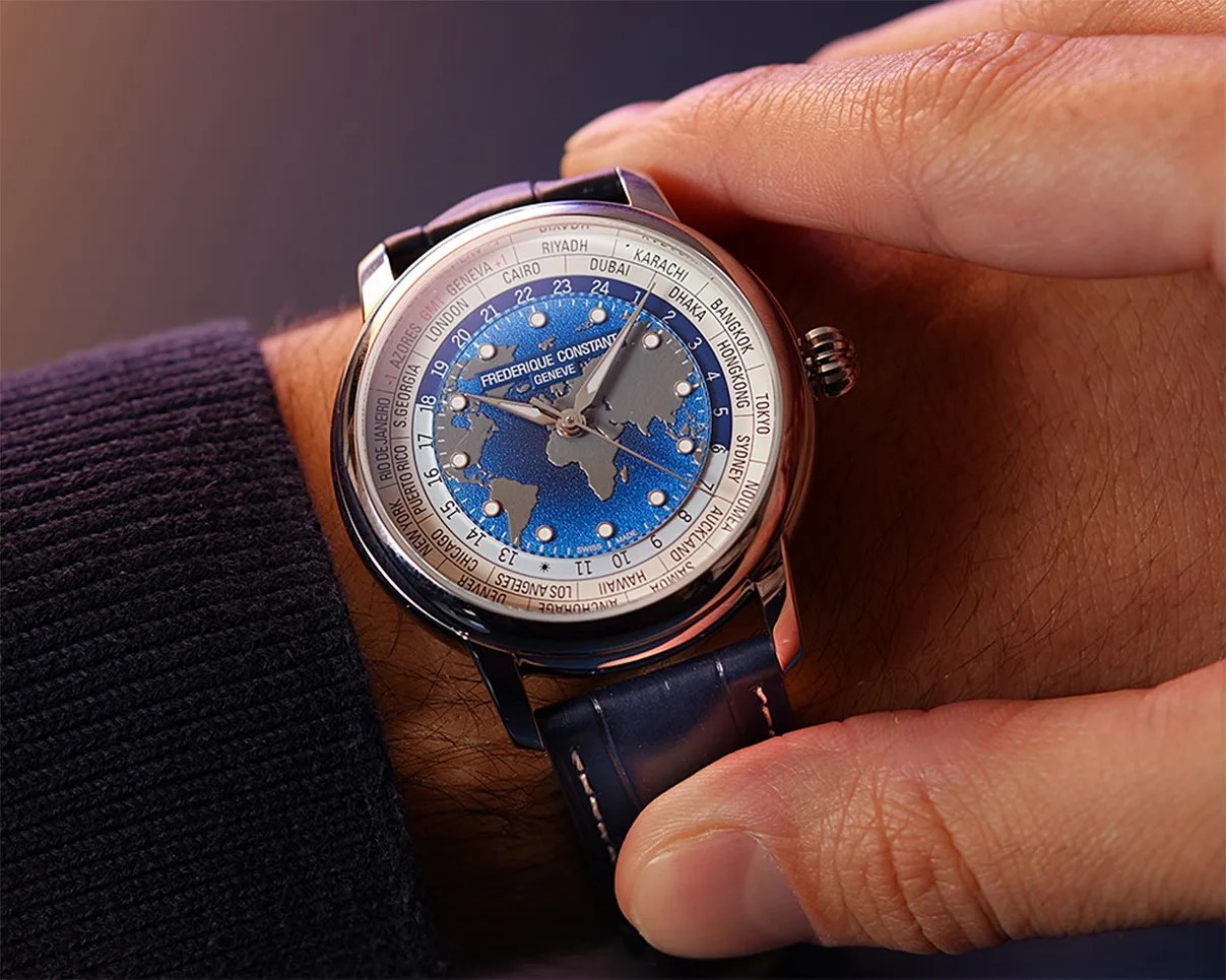 Silver Frederique Constant wristwatch with blue world map dial and blue leather strap worn on a wrist.