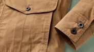 Close-up of tan cotton jacket sleeve and pocket with black buttons labeled "C.C. Filson Co. Seattle.