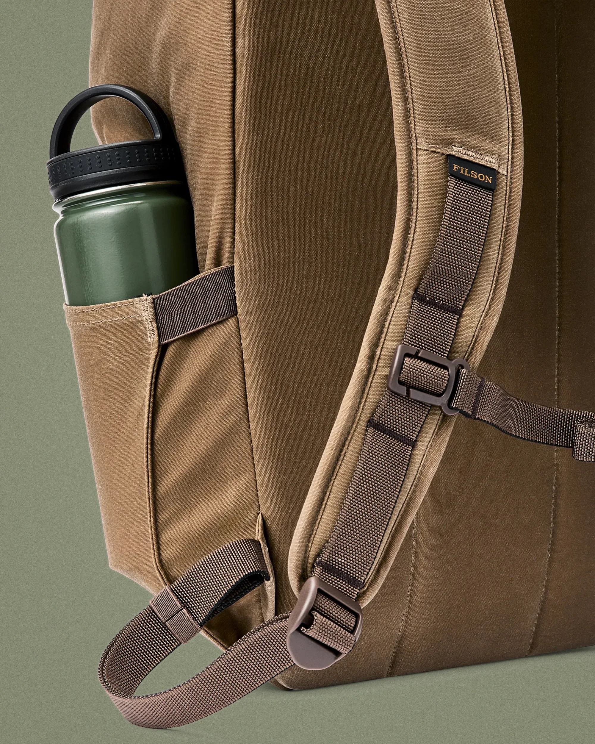 Brown canvas backpack with padded straps and a green water bottle in a side pocket.