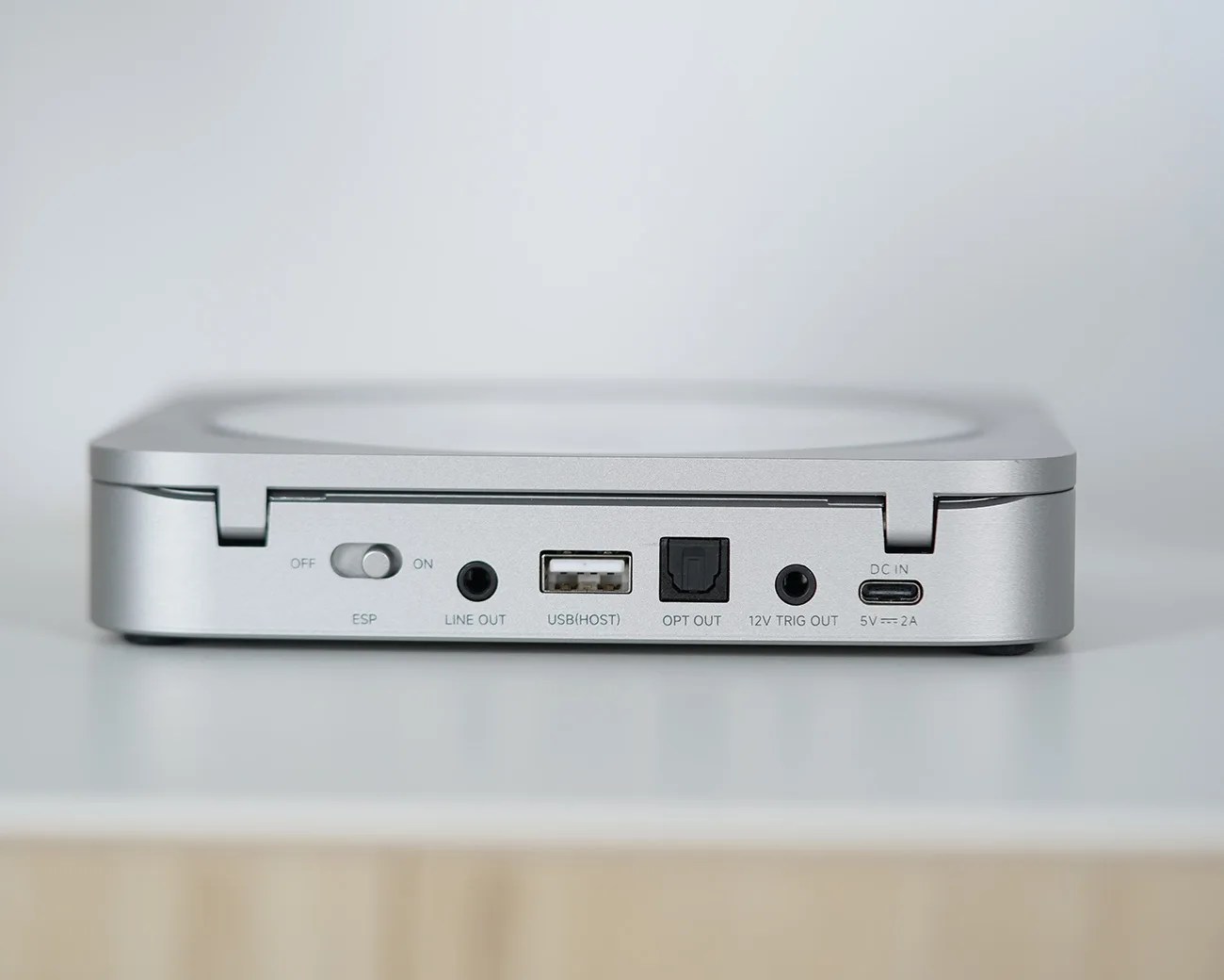 Silver electronic device with USB, optical, line out, 12V trigger, and DC power ports on a white surface.