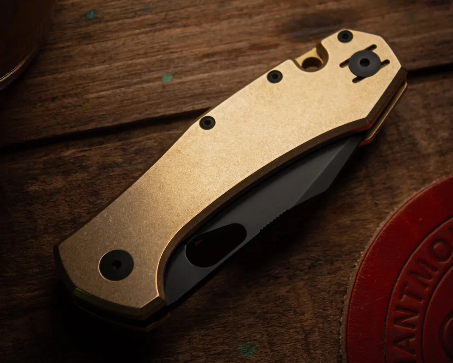 Folded pocket knife with a gold-colored handle and a partially visible black blade on a wooden surface.